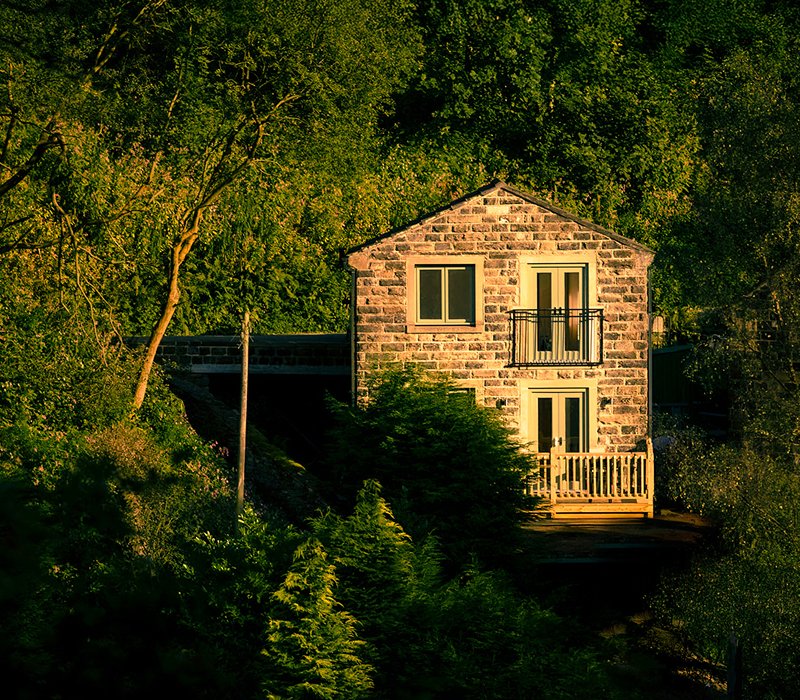 Stone house surrounded by lush green trees and foliage, with a small balcony and wooden porch.