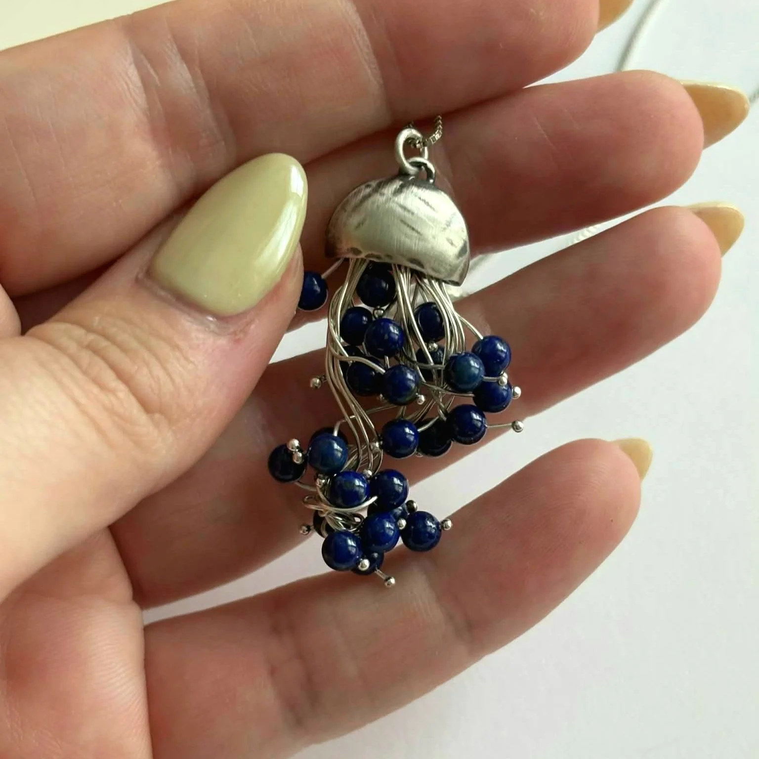 Hand holding 18" sterling silver necklace with jellyfish pendant with dark blue pearls