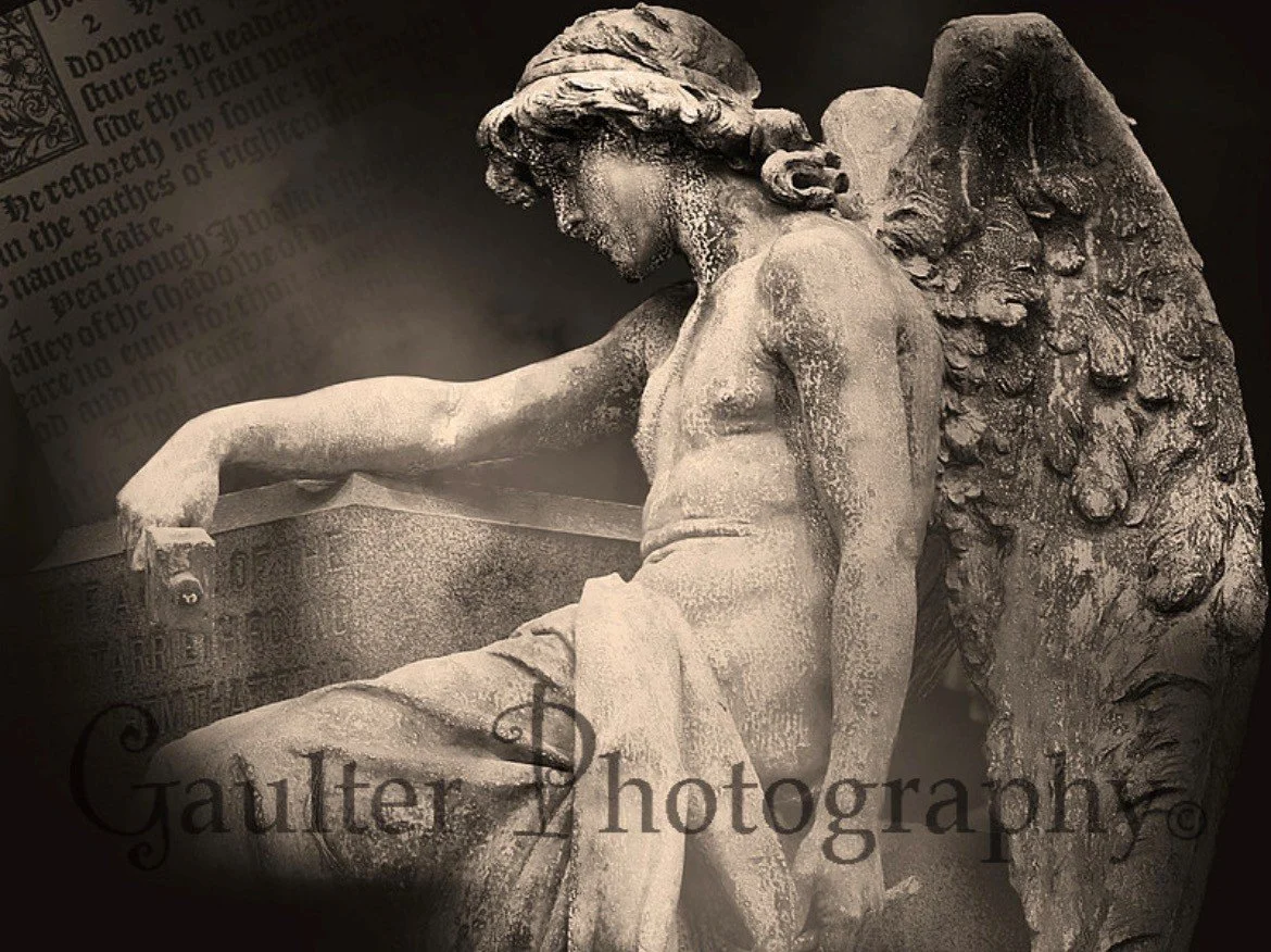 A weathered stone sculpture of a kneeling angel with large, detailed wings. The angel's head is bowed and has a serene expression. Background features a blurred open book and text.