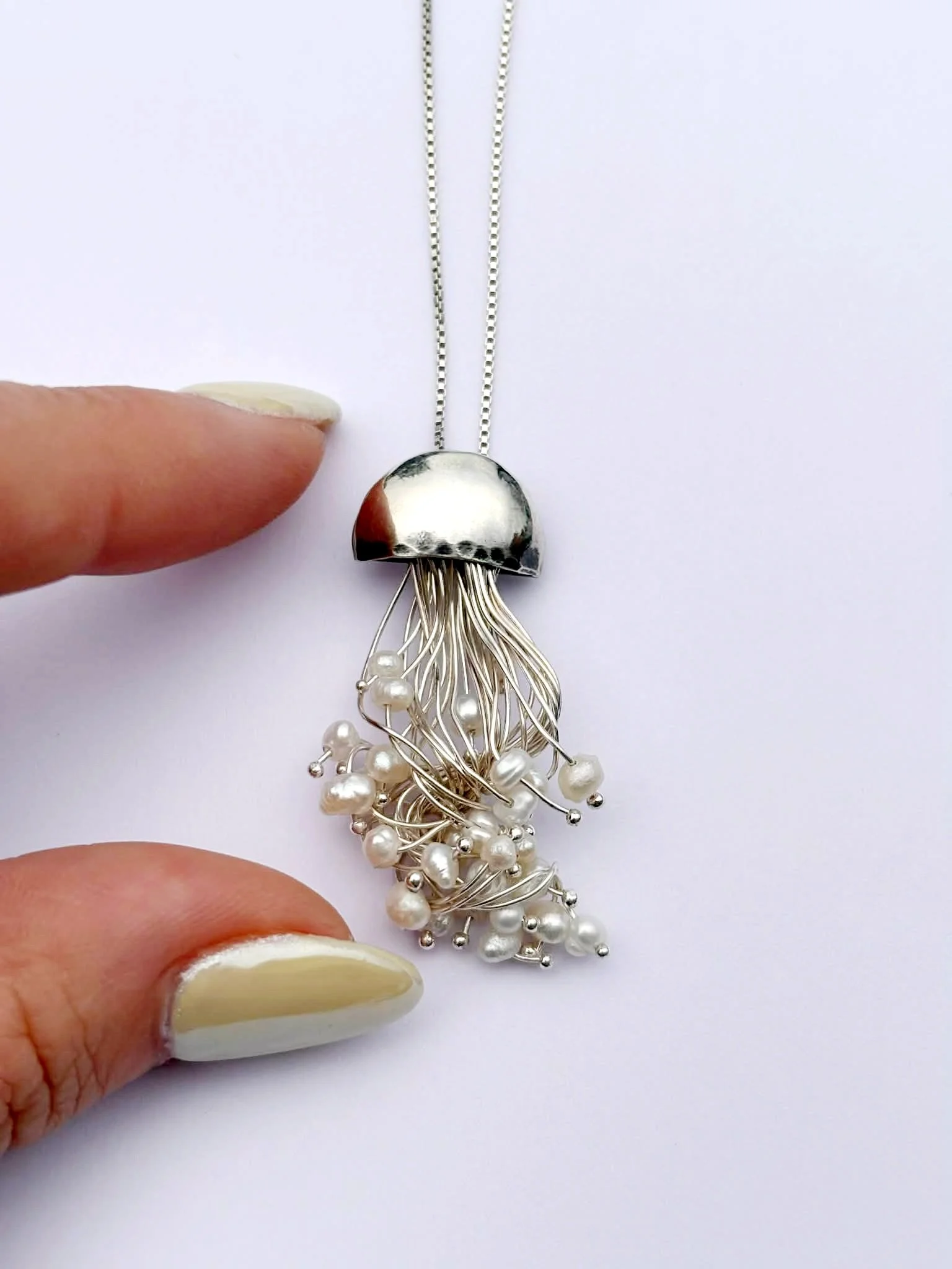 Hand holding 18" sterling silver necklace with jellyfish pendant with white pearls
