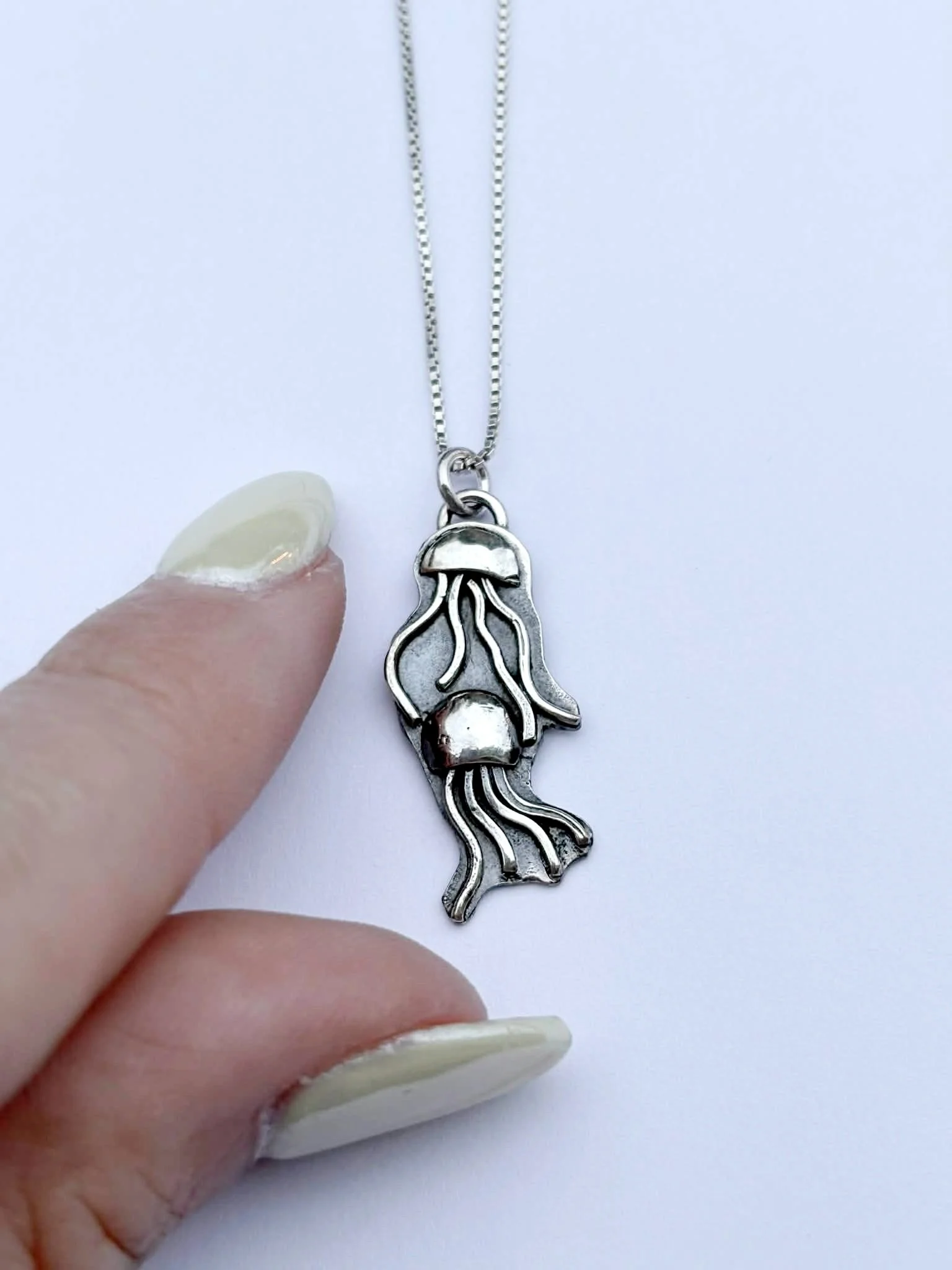 finger next to 18" sterling silver necklace with a  2  jellyfish pendant with polished tentacles and darkened background