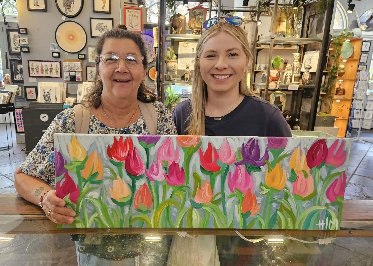 Two women holding  a painting of tulips they purchased