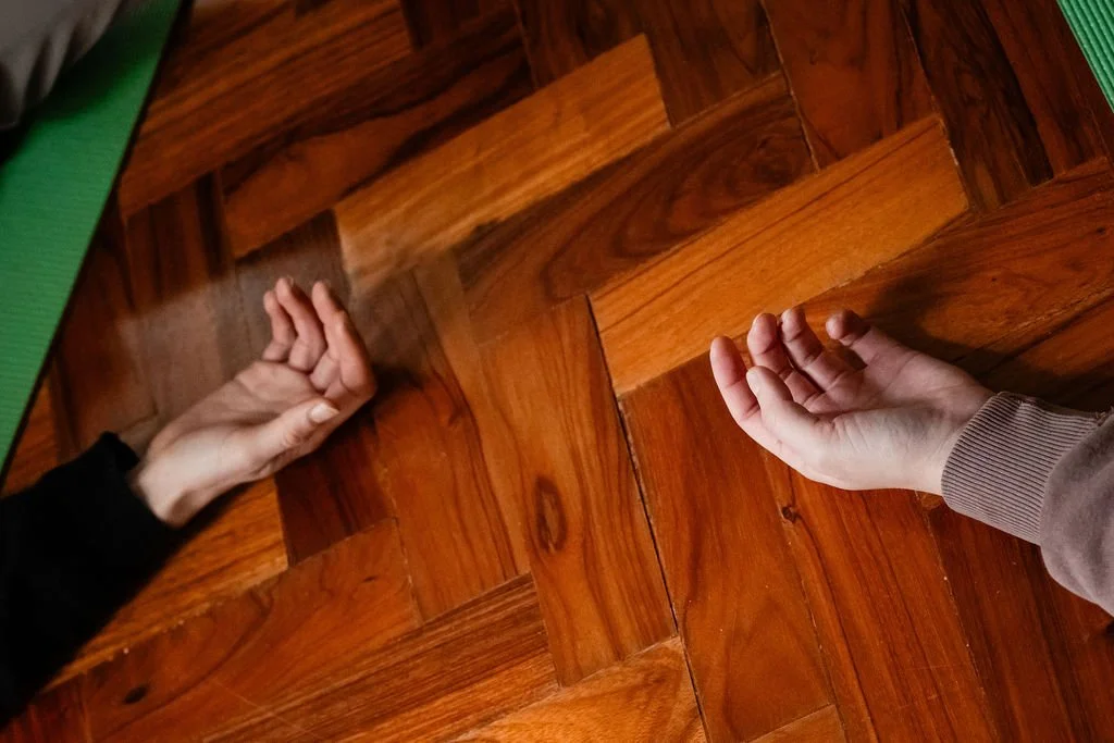 two hands resting on wooden floor with palms facing upwards. There´s a cosy and relaxed atmosphere