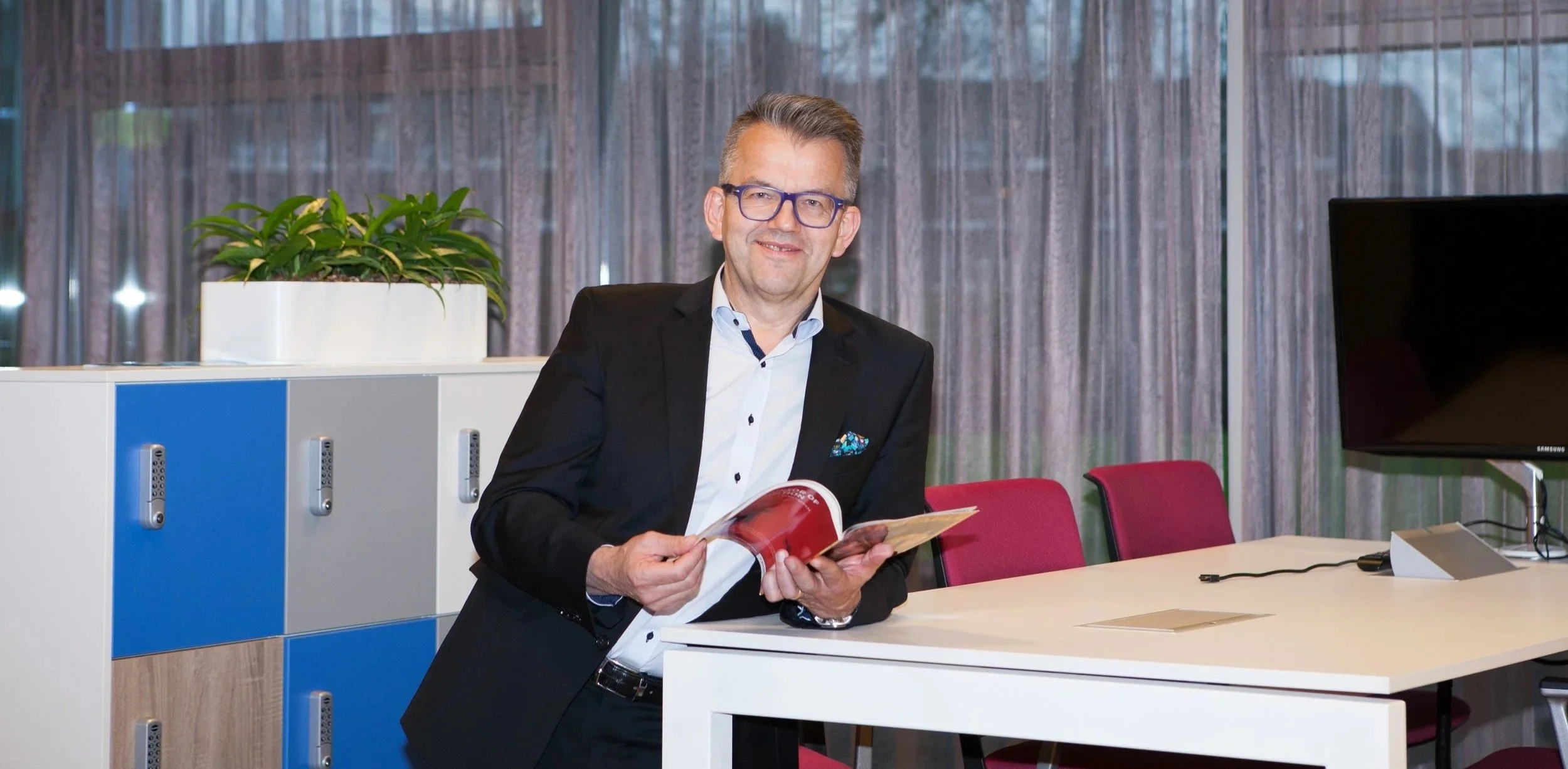 Ein Mann in einem schwarzen Anzug liest in einem Magazin in einem modernen Büro.