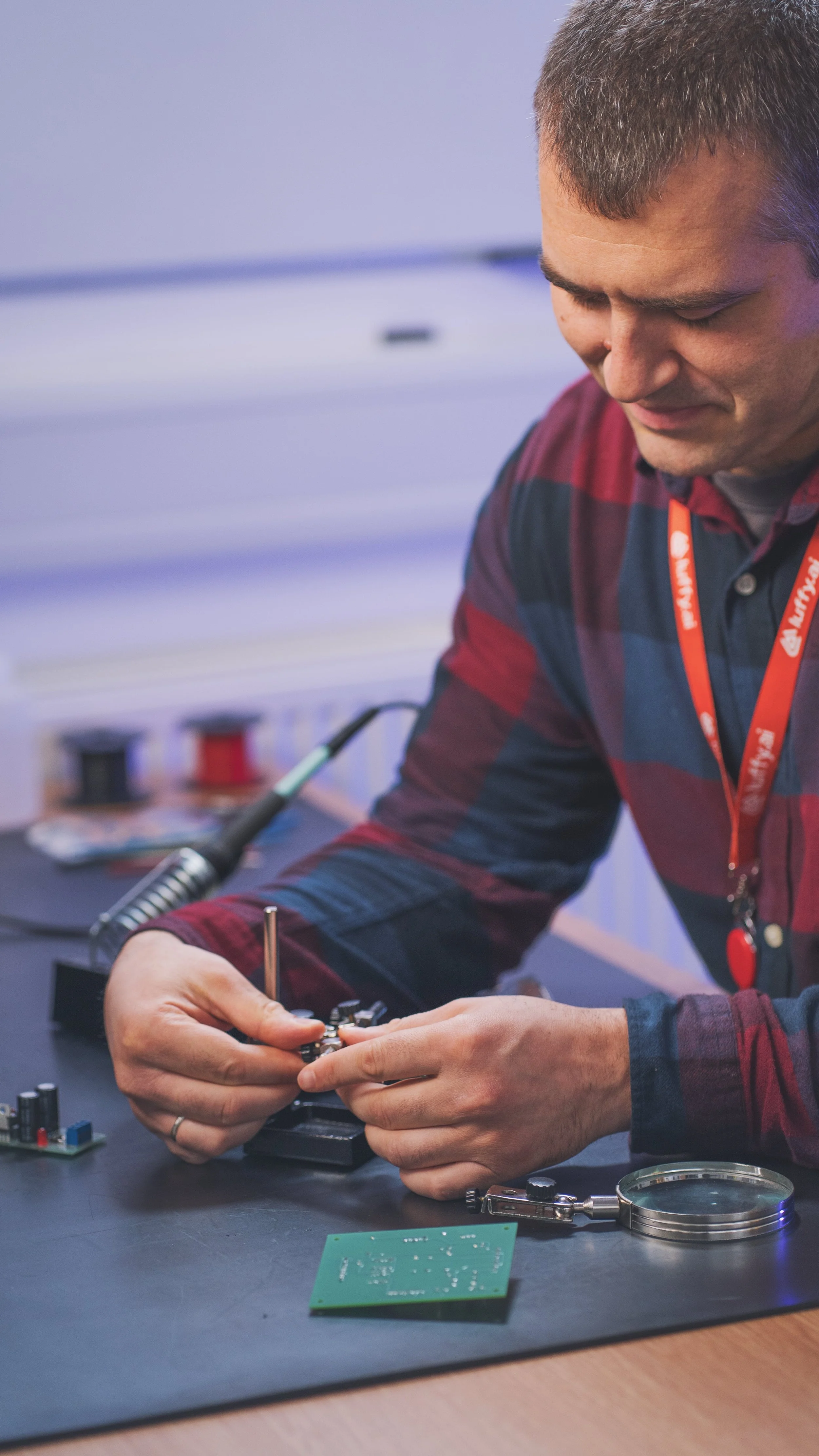 A person working on a circuit board at a workbench with electronic tools and components.