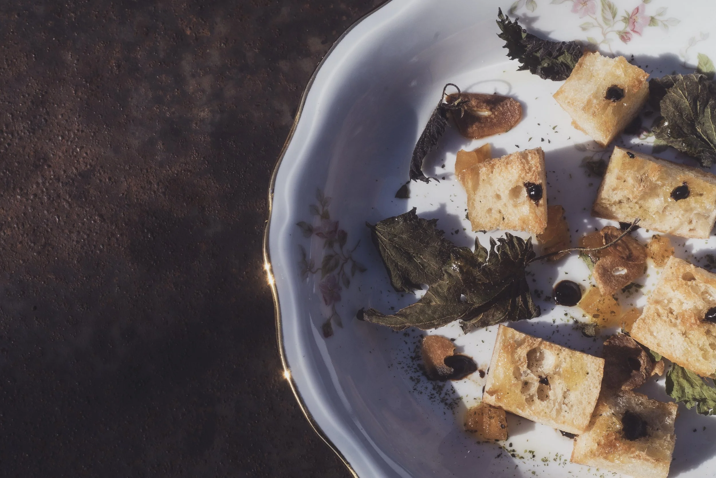 Restes de pain grillé, feuilles de menthe, et quelques gouttes de sauce sur une assiette en porcelaine avec un motif floral, vue partielle.