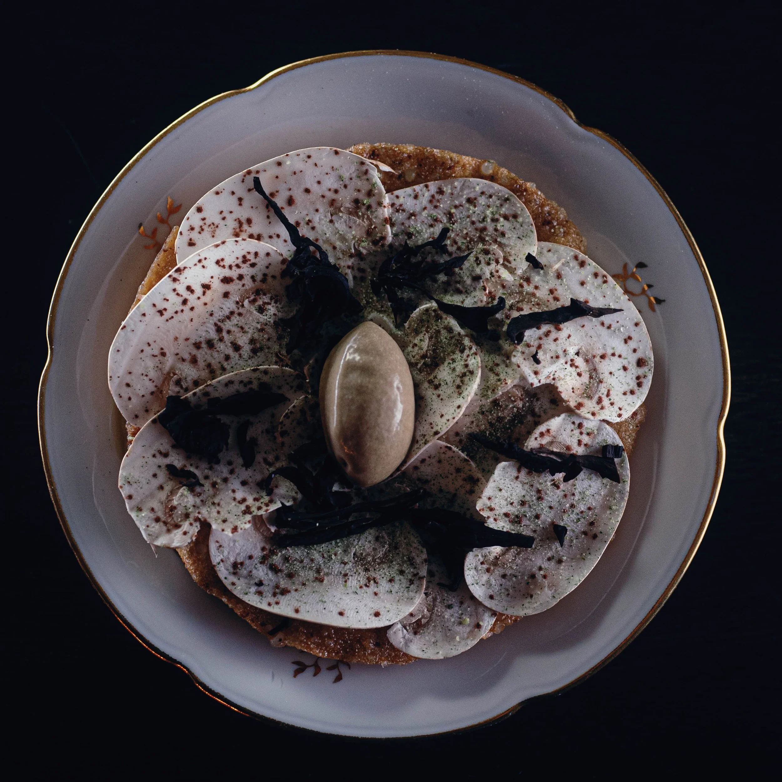 Dessert avec des tranches de poires, une boule de glace ou de crème, et des morceaux de chocolat noir sur une assiette ornée d'une fine line dorée.