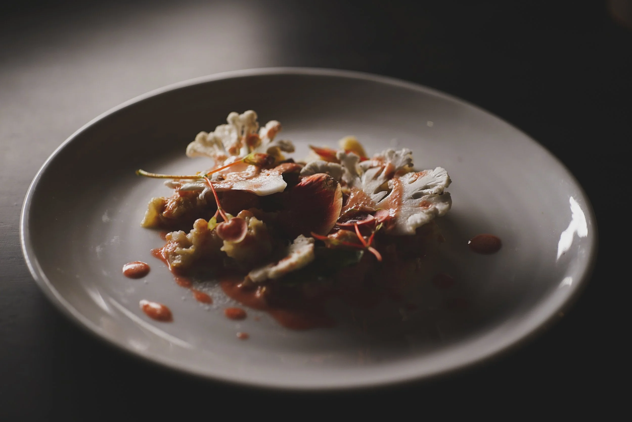 Assiette de nourriture avec des tranches de viande, une sauce, des légumes et des micro-pousses.