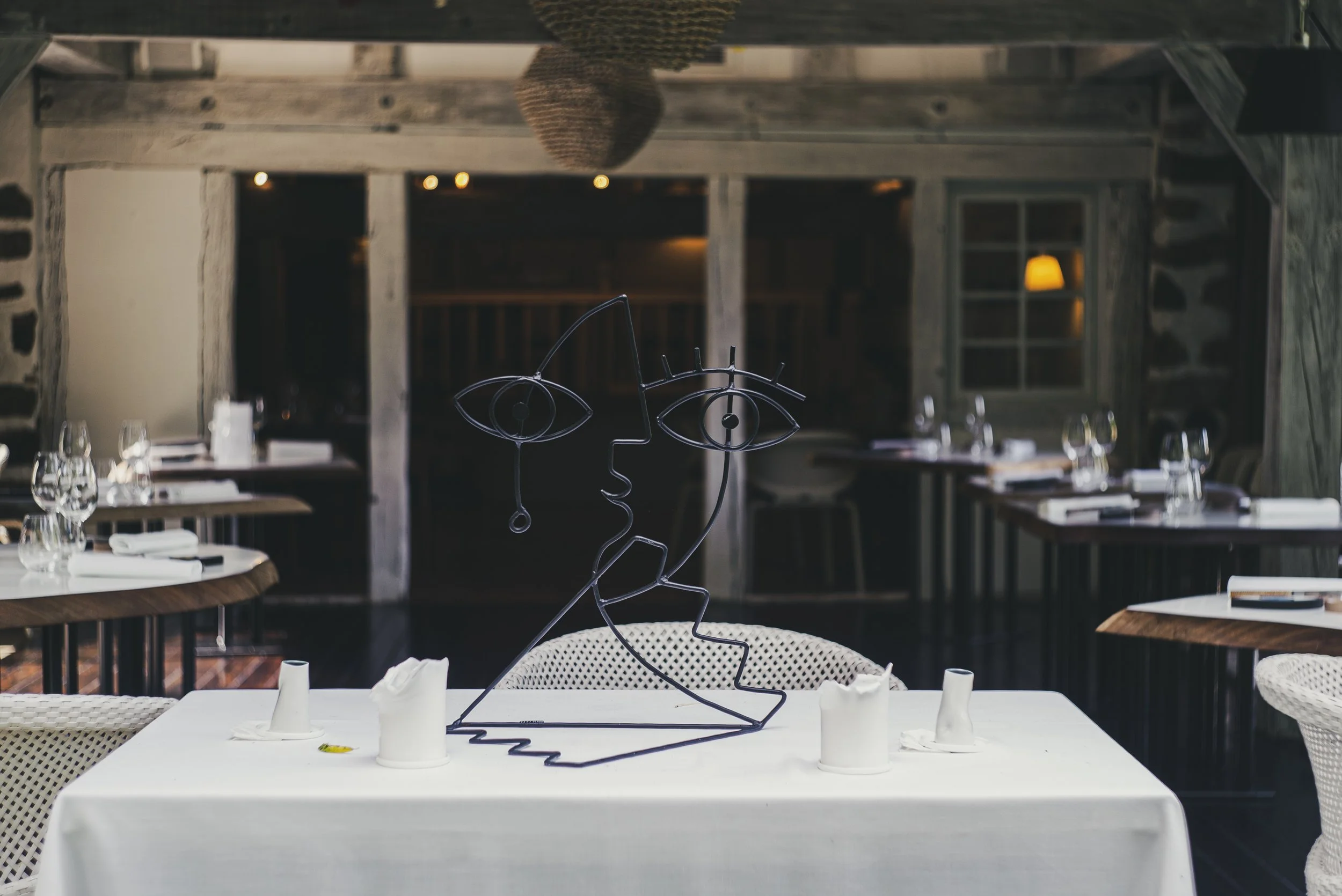 Décoration de table avec sculpture en fil de fer représentant un visage humain, dans le restaurant Le Moulin d'Alotz avec tables élégantes et ambiance chaleureuse.