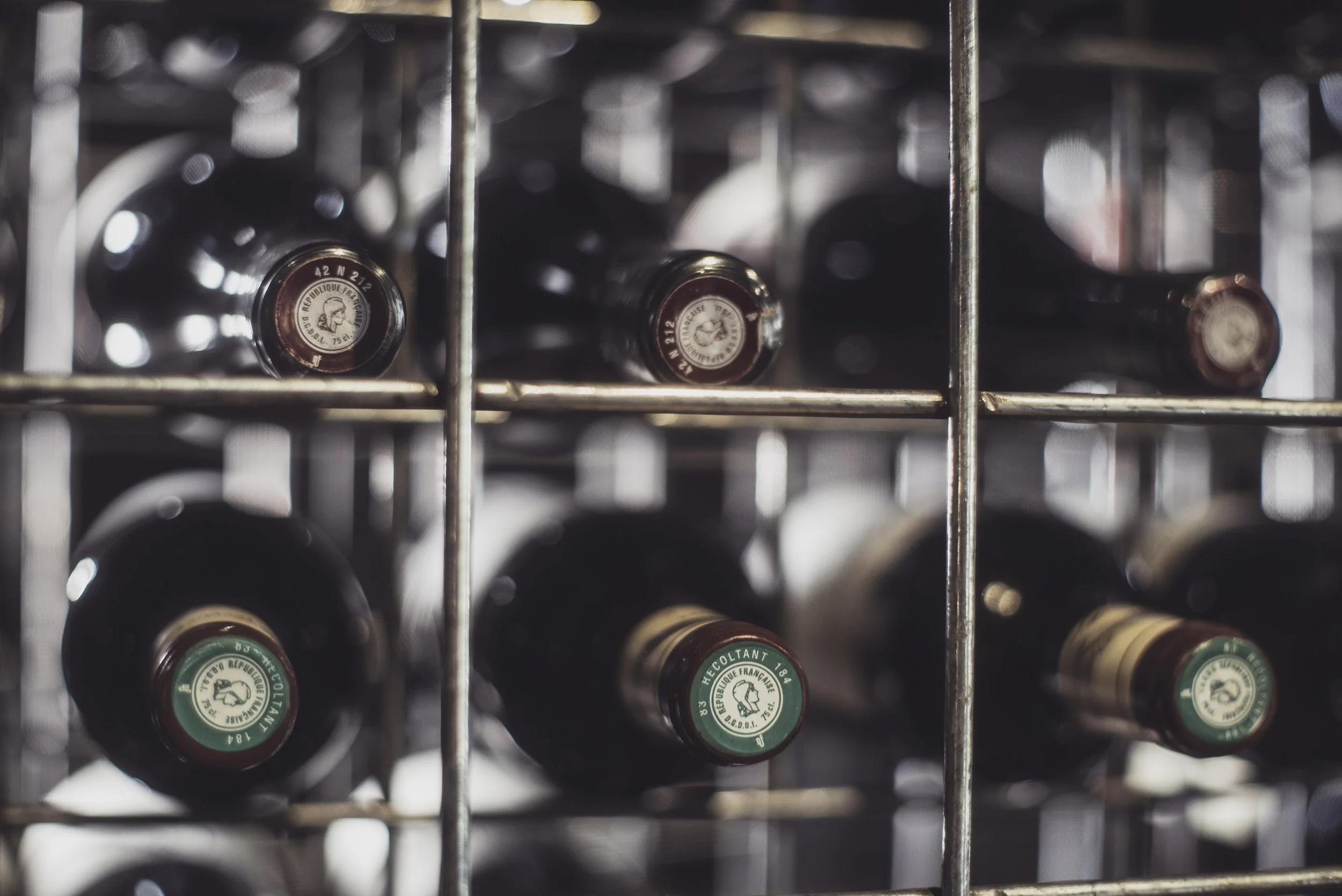 Bouteilles de vin stockées horizontalement dans une cave à vin, séparées par une grille en métal.