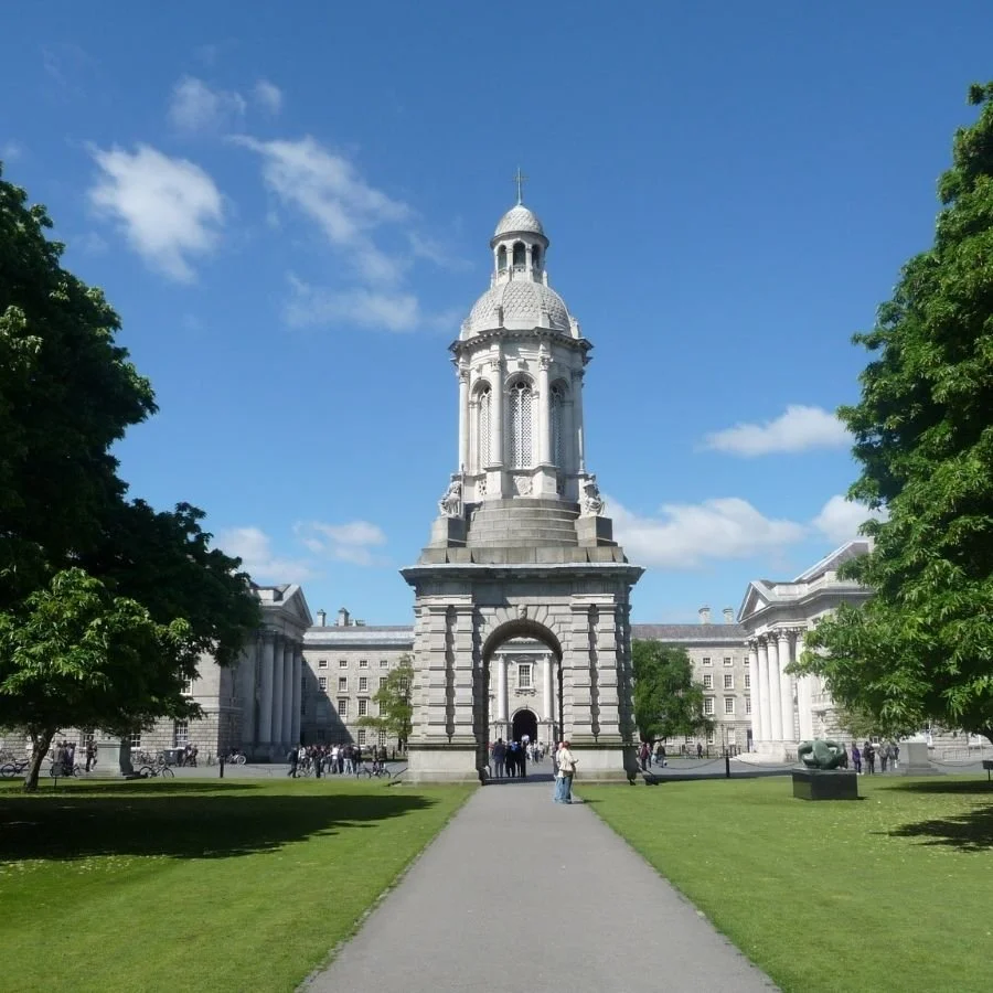 Historical building with a tall dome, columns, and an archway entrance surrounded by green grass and trees under a blue sky.
