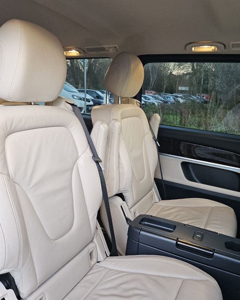 Interior of a vehicle showing beige leather seats, a black center console, and a window revealing parked cars outside.