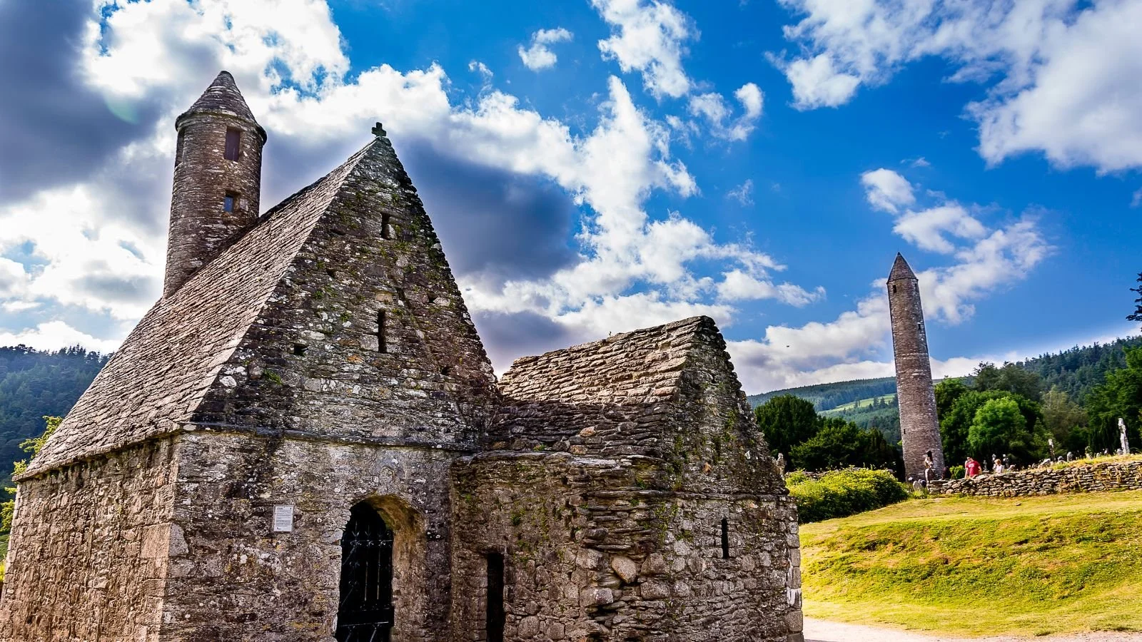 An old stone church with a tall, narrow tower in a rural landscape under a partly cloudy sky.