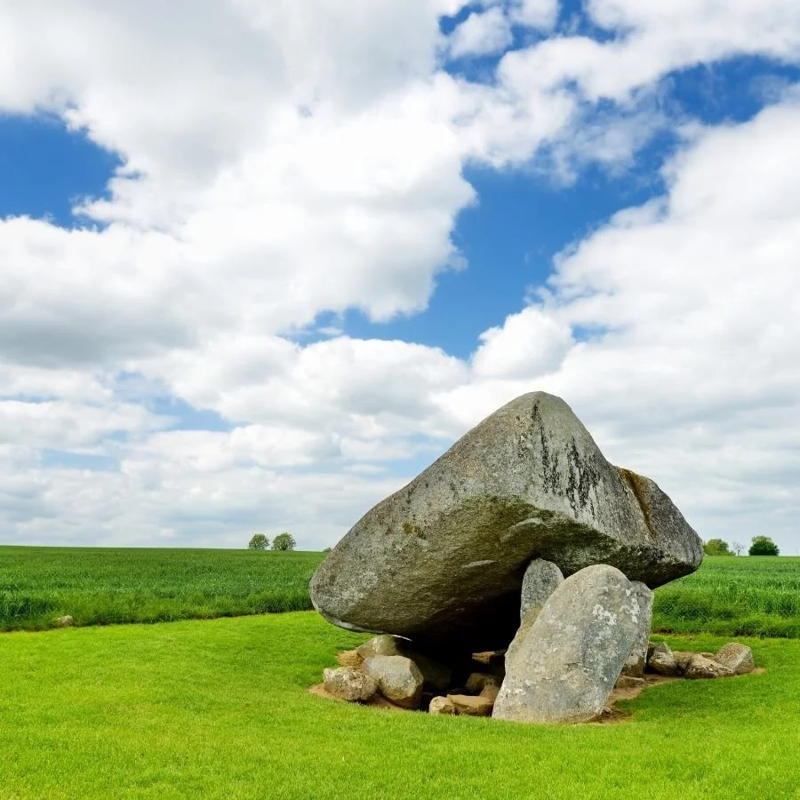Large ancient stone formation in a grassy field with a partly cloudy sky.