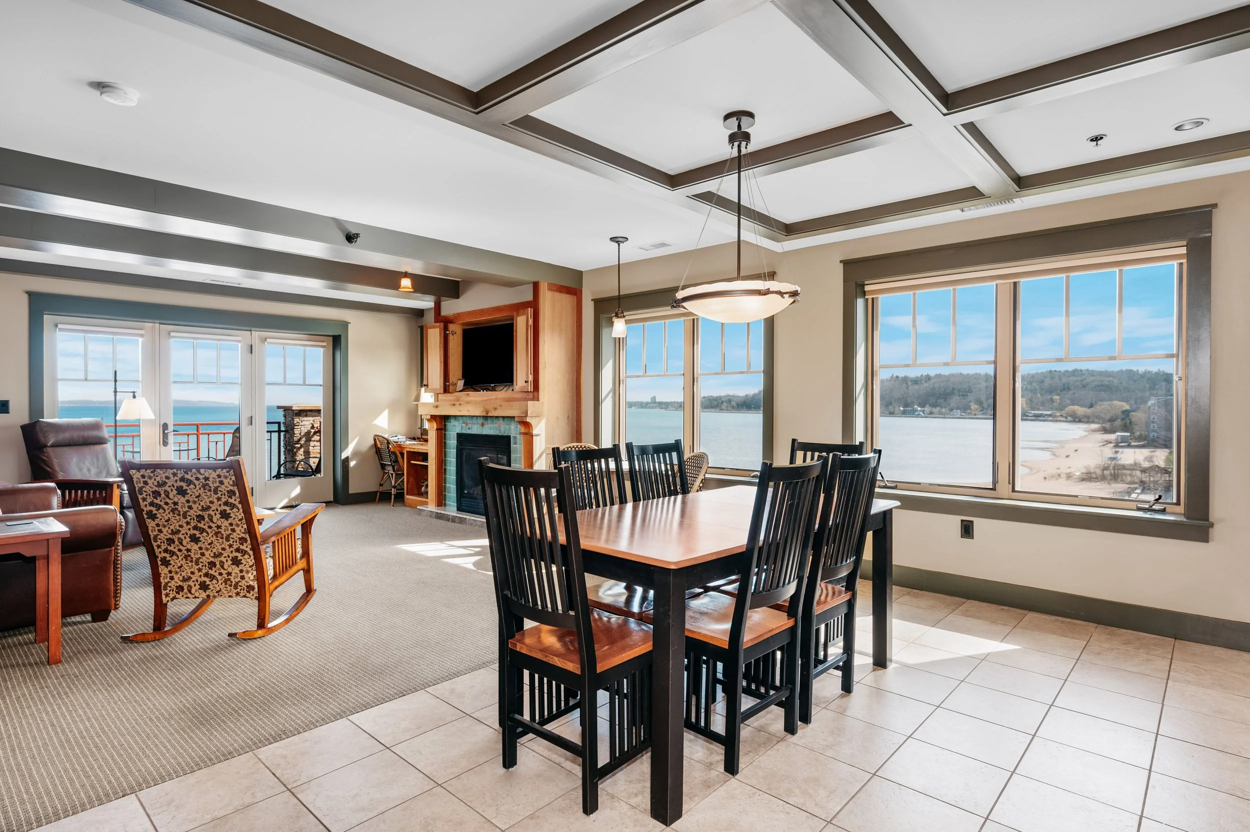 Living and dining area with windows overlooking a lake, a fireplace, dining table with chairs, and a sliding glass door leading to a balcony