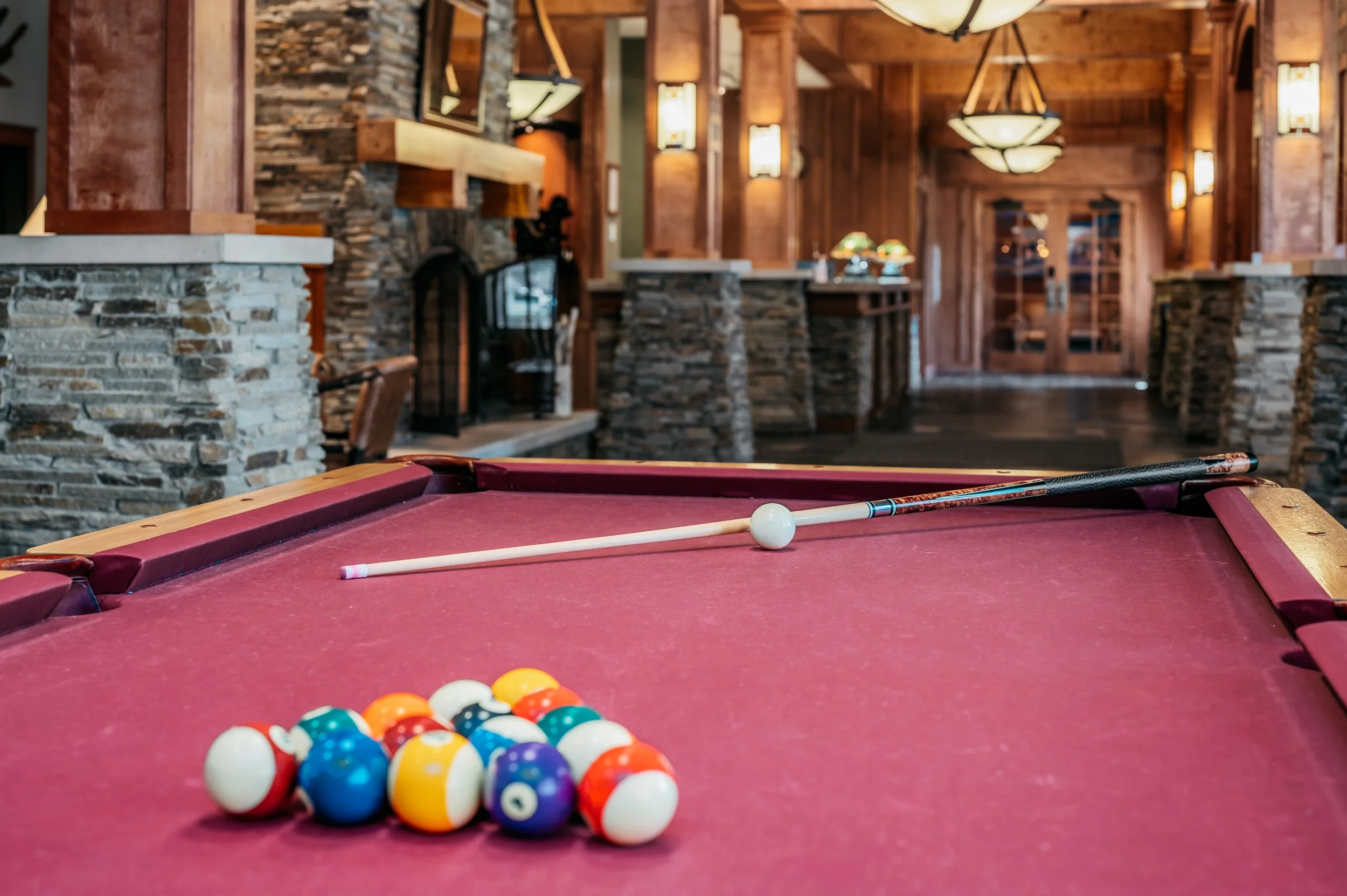 A pool table with a cue stick and a set of billiard balls in a cozy, wood-paneled game room.