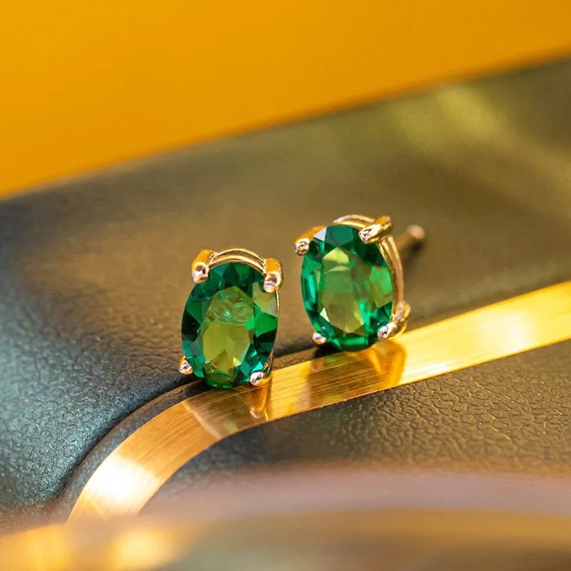 Pair of emerald green gemstone earrings with silver prongs on a textured black and gold surface.