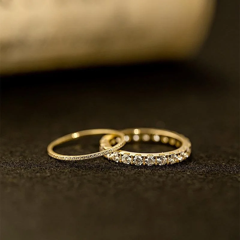 Two gold rings, one with diamonds, placed on a black surface.