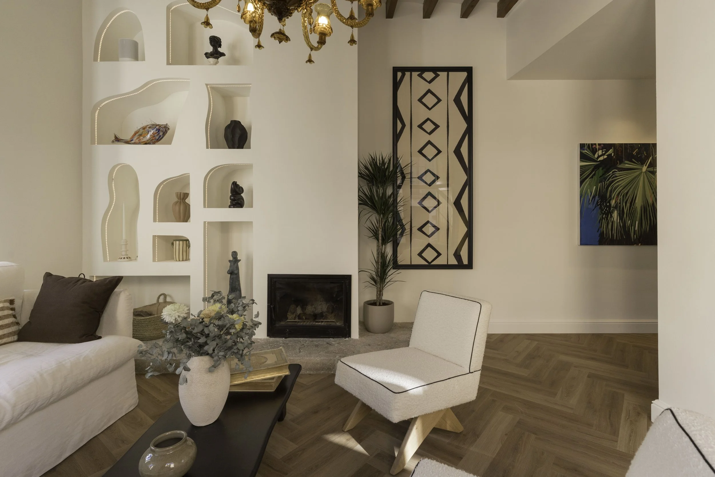 Sala de estar moderna con chimenea, plantas, obras de arte en las paredes y muebles blancos y beige.