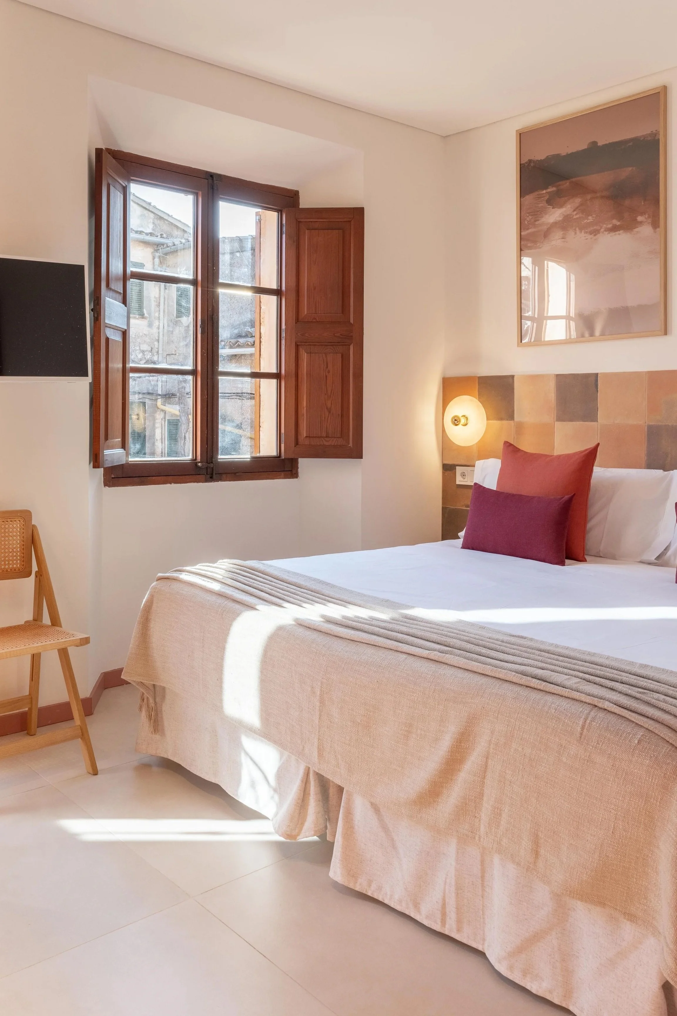 Habitación con cama, almohadas, ventana de madera y decoraciones cálidas.
