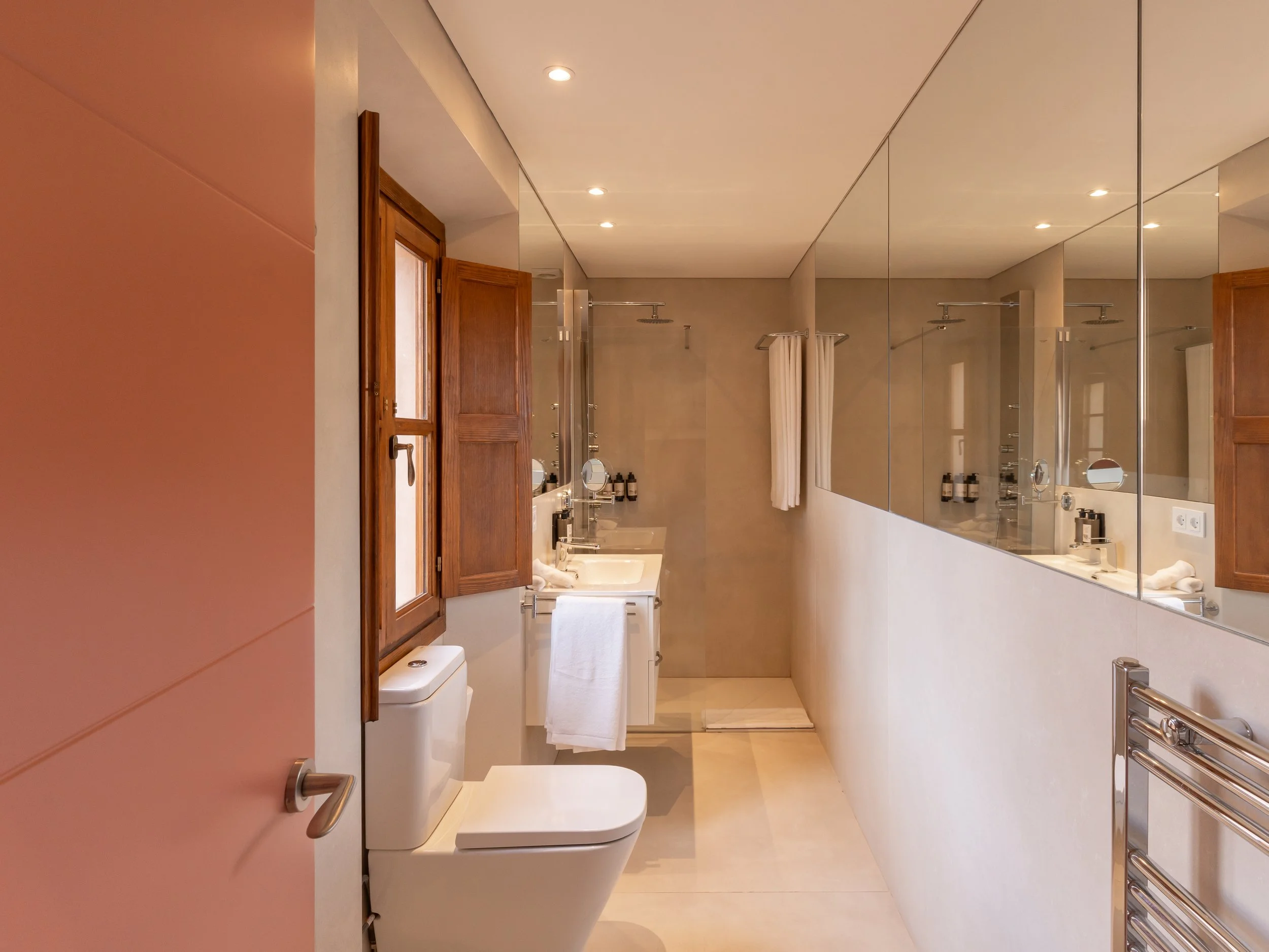 Baño moderno con lavabo, espejo grande, ducha y ventanas de madera.