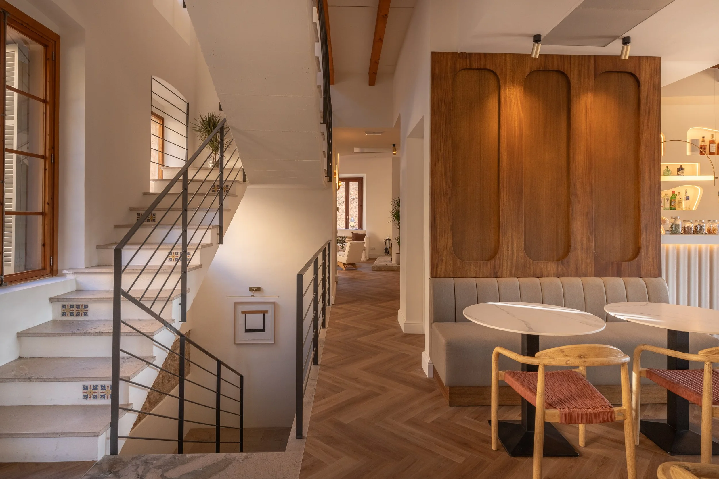 Interior de un restaurante o cafetería con escaleras, mesas y sillas, decoraciones en madera y plantas.