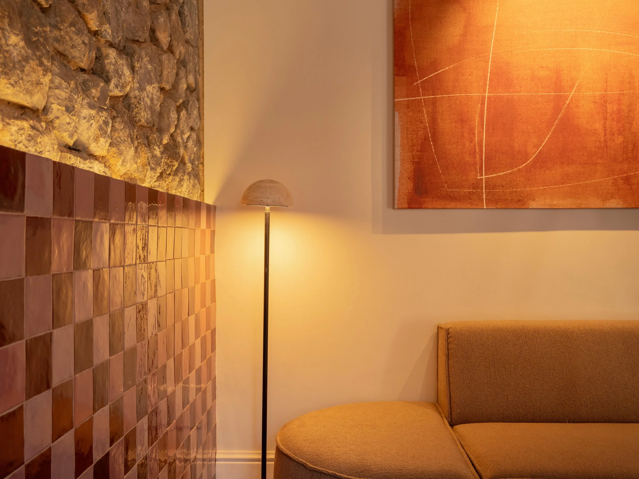 Sala con pared de piedra, lámpara de piso, cuadro con arte abstracto naranja y mueble con tapizado beige.