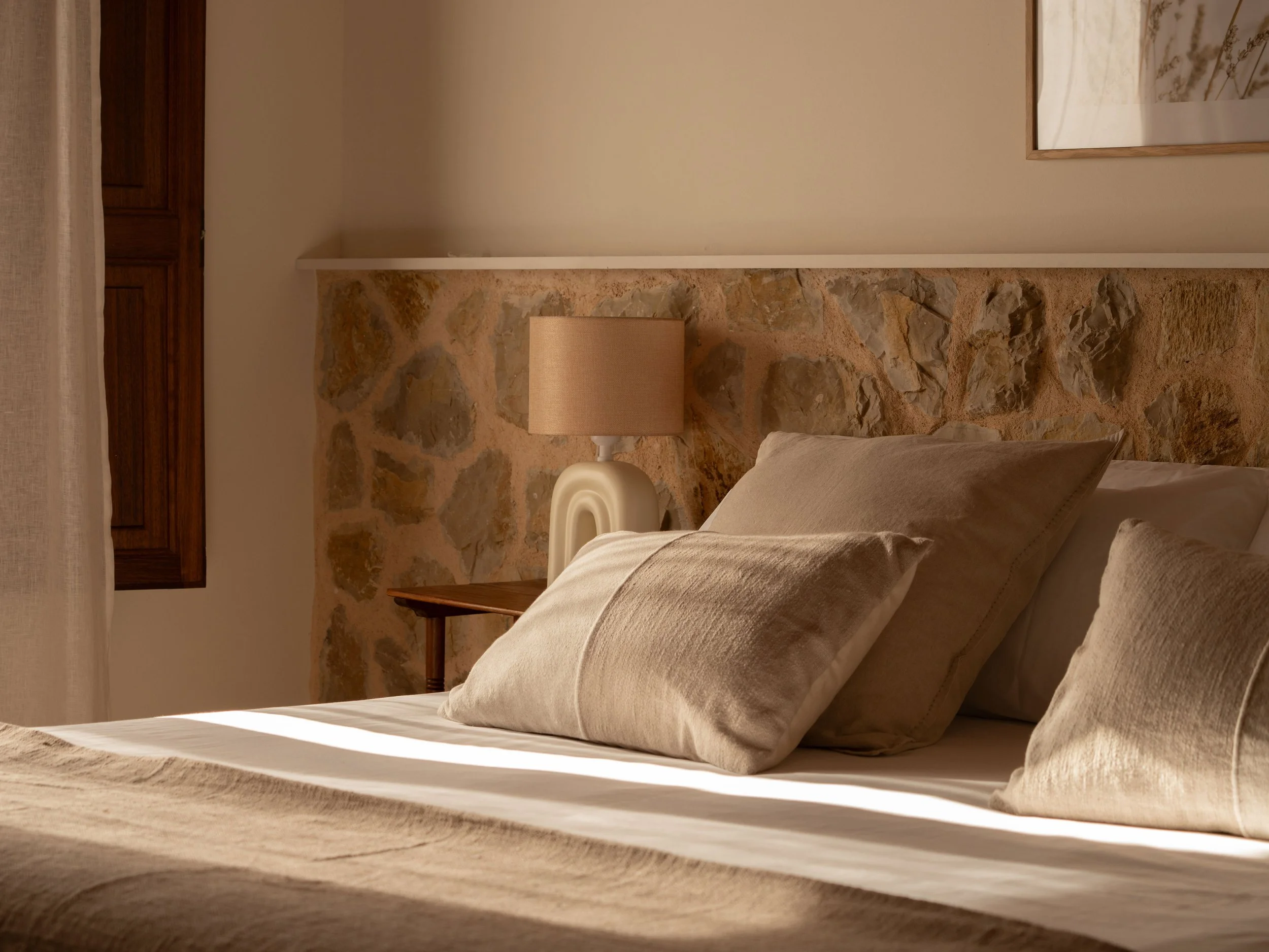 Cama con almohadas y lámpara en una habitación con pared de piedra.