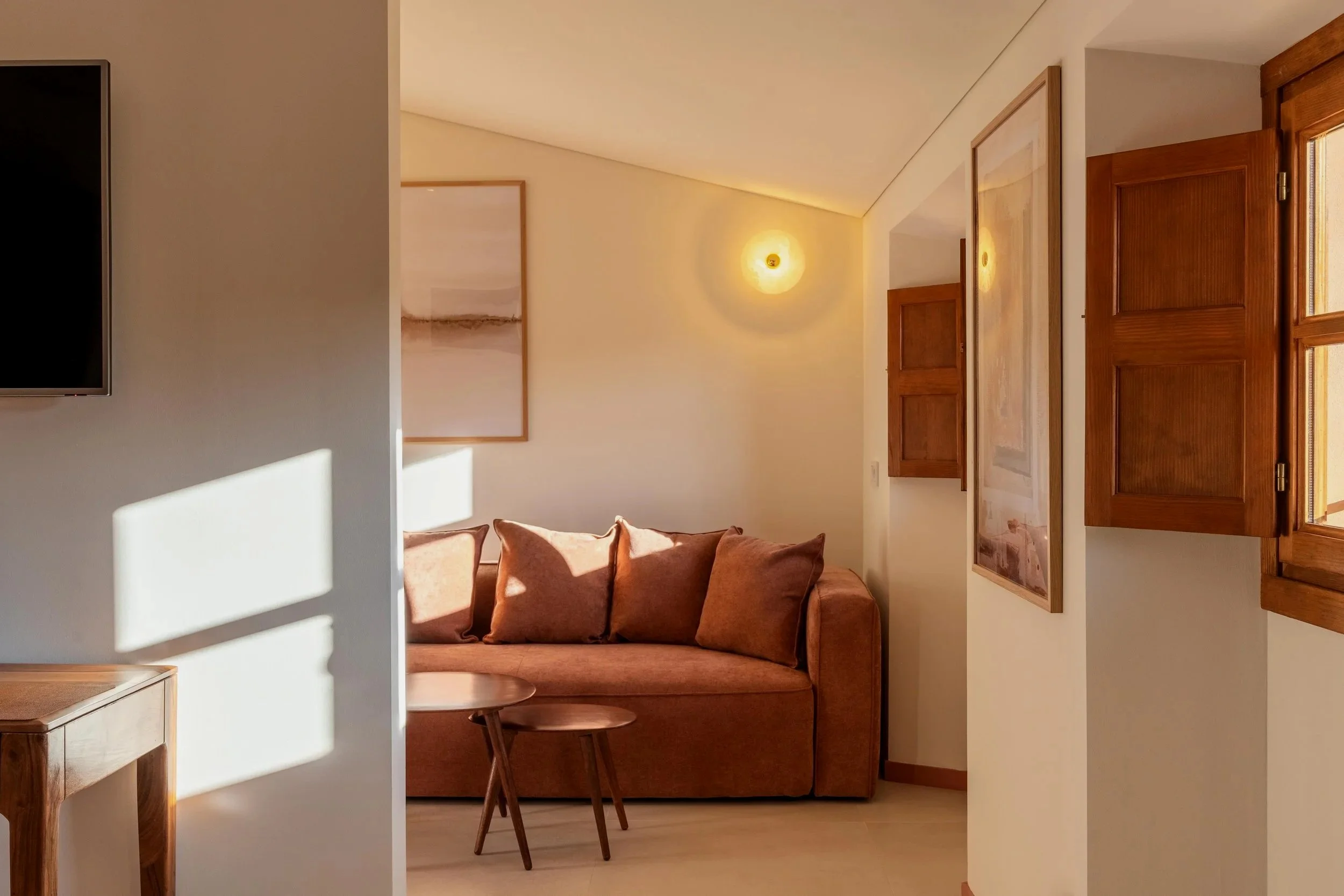 Sala de estar con sillón de color terracota, ventanas de madera, cuadros en la pared y luz cálida