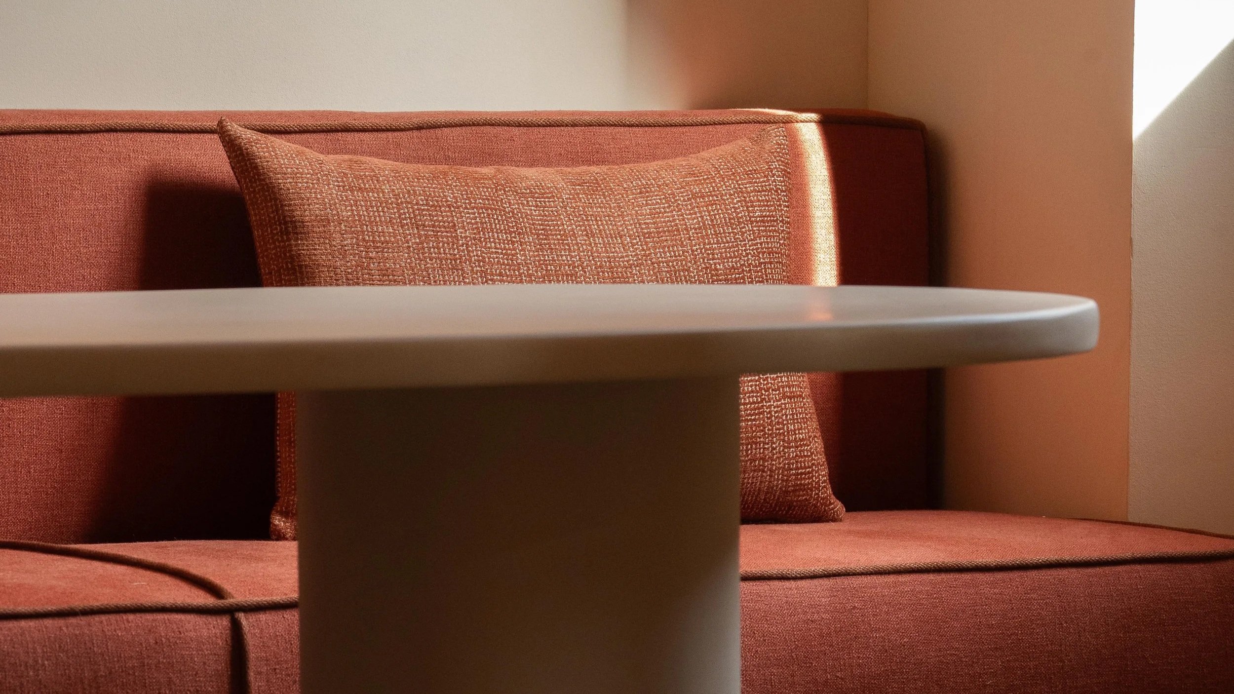 Sofá de color rojo con cojines, y una mesa redonda blanca en primer plano.