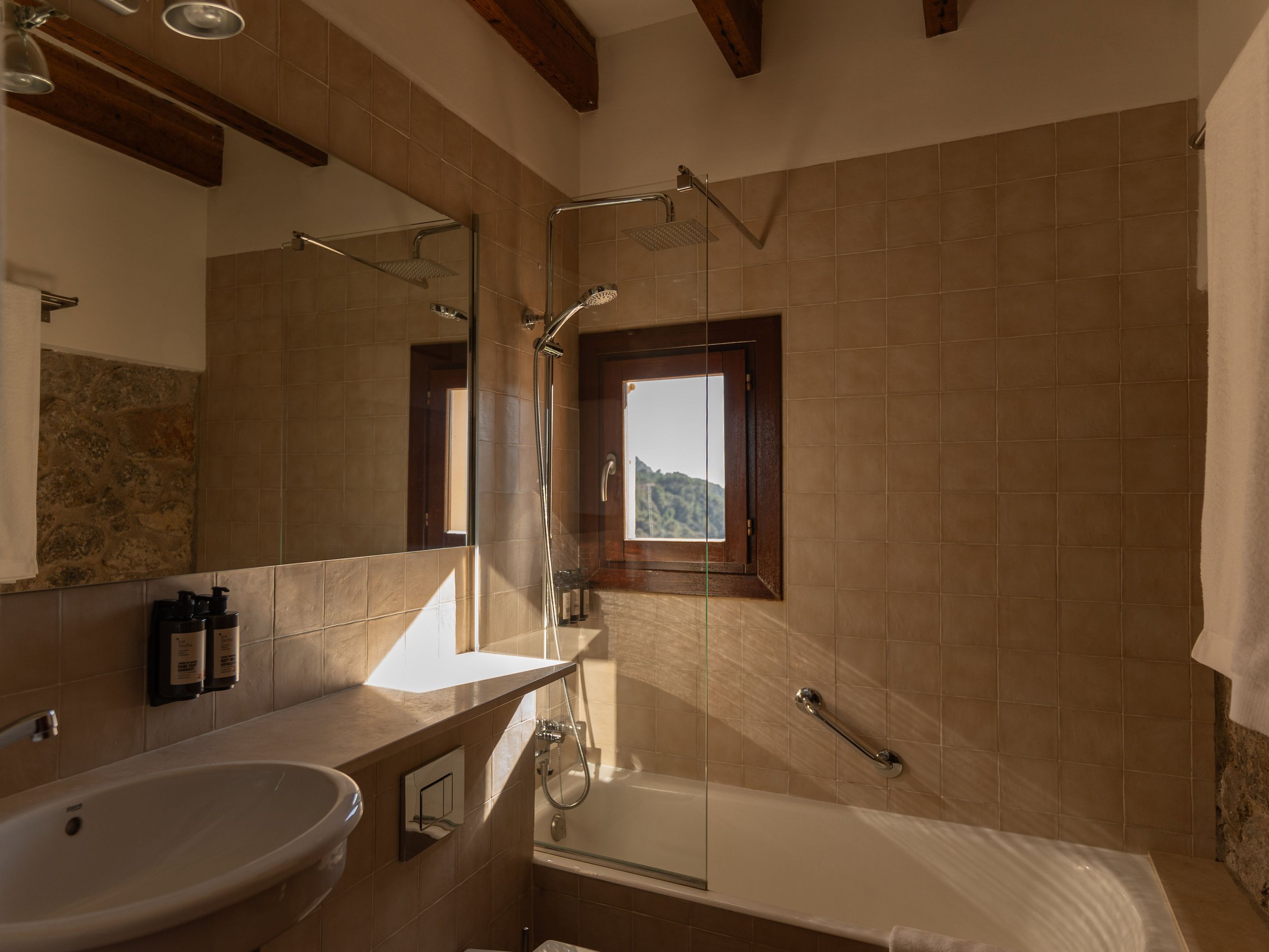 Baño con lavabo, espejo, ducha con mampara y ventana con vista a un paisaje natural.