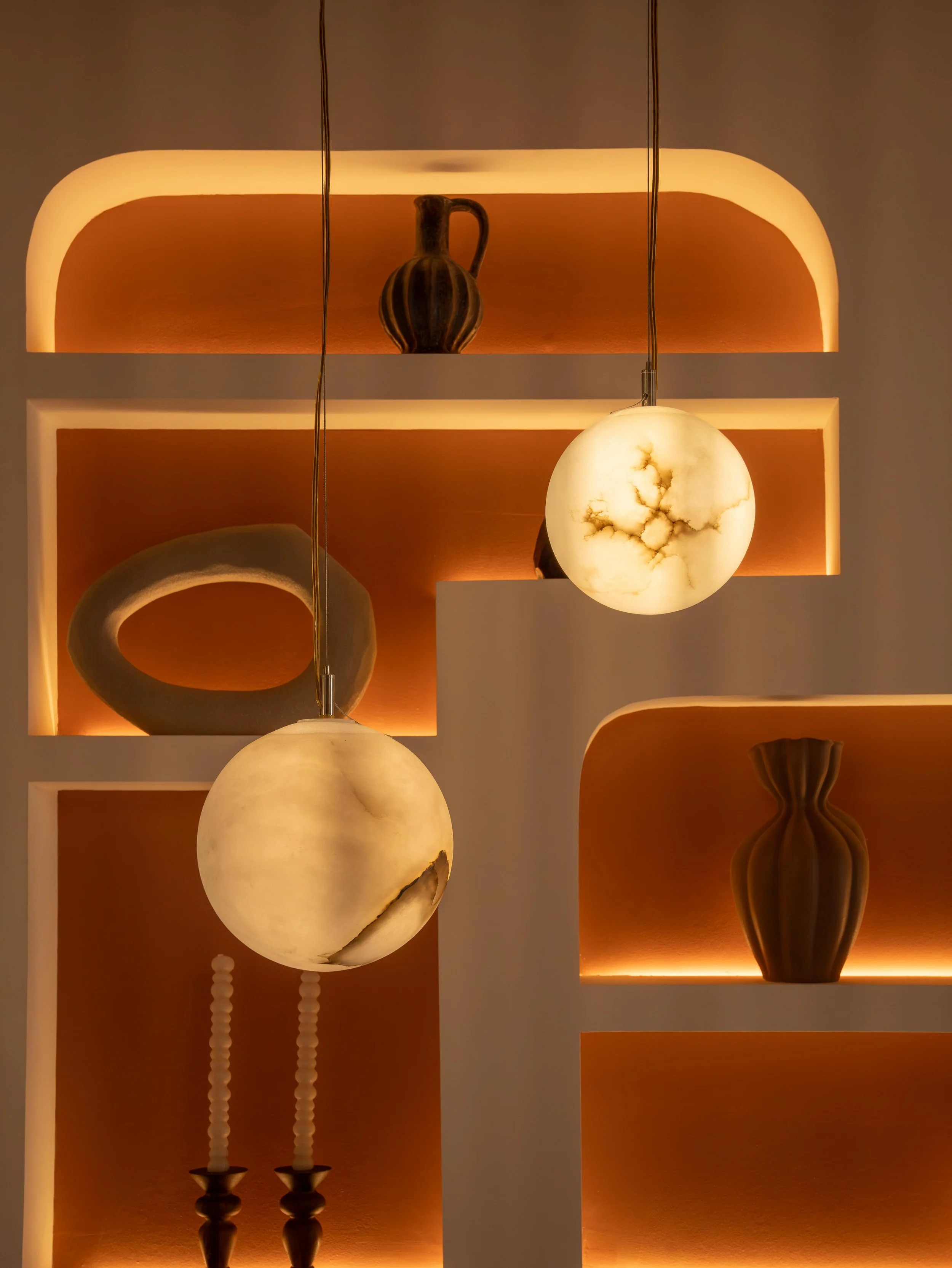 Estanterías con iluminación cálida que exhiben jarrones de cerámica y una lámpara de bolas de piedra en un espacio decorativo.