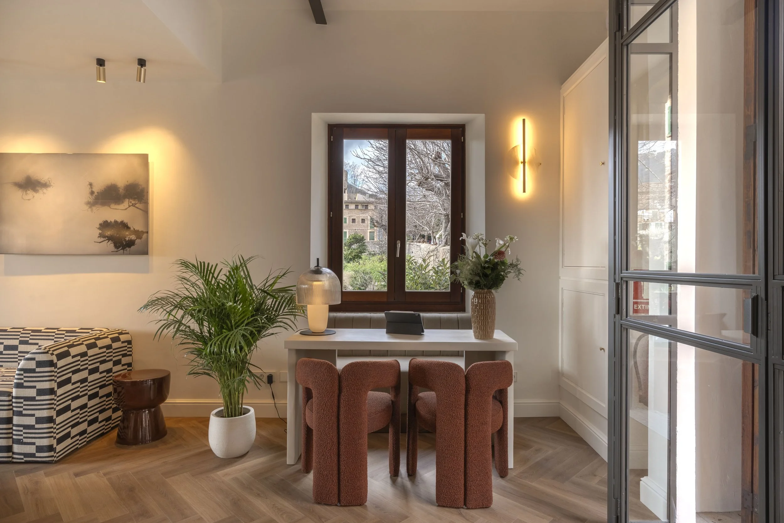 Interior de un salón con sillones, plantas, mesa de comedor, ventana y decoración moderna con luz cálida