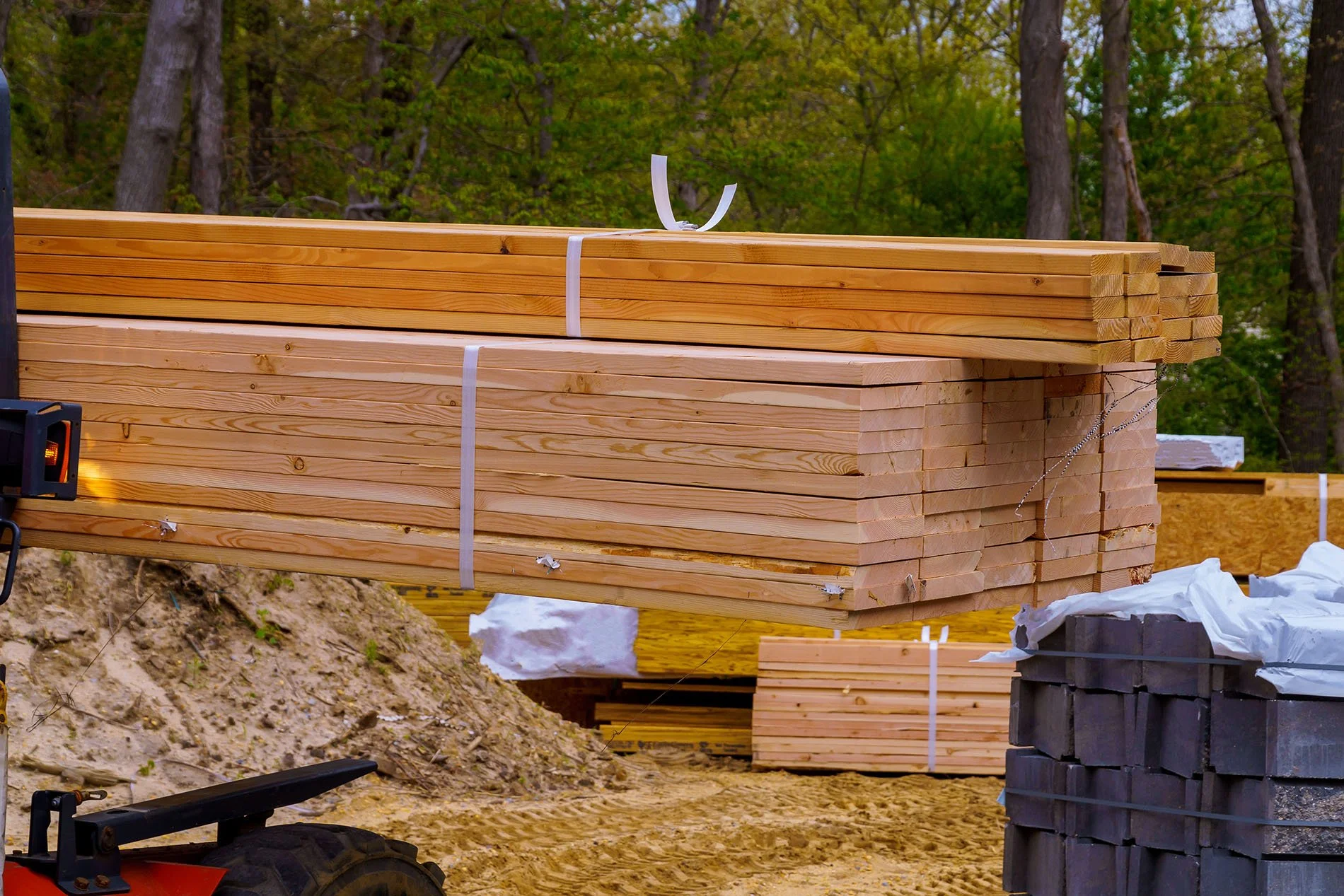 Stacks of cut lumber at a construction site surrounded by trees.