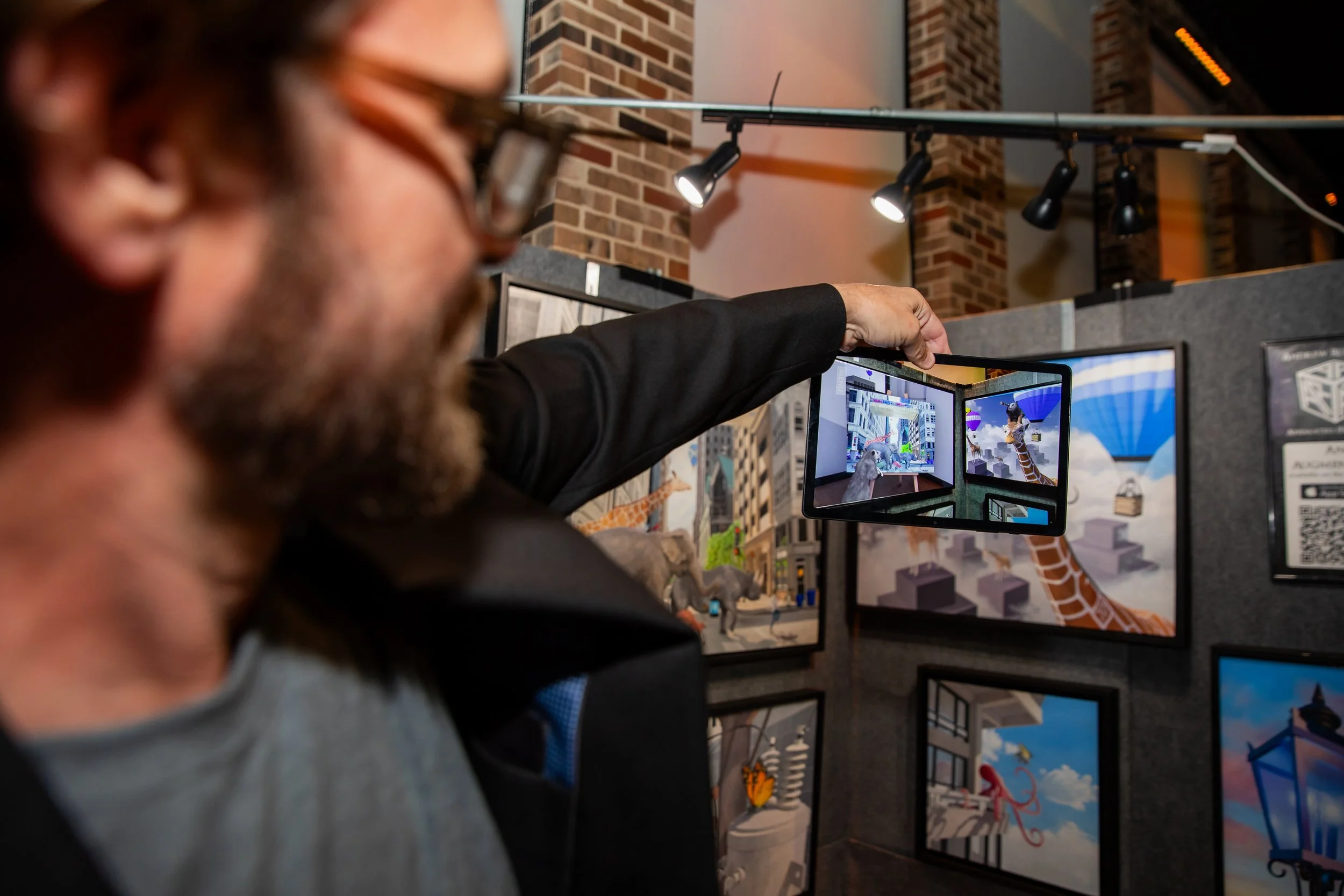Person pointing at digital screens displaying 3D models, with other screens showing architectural and design images, in an indoor exhibition setting.