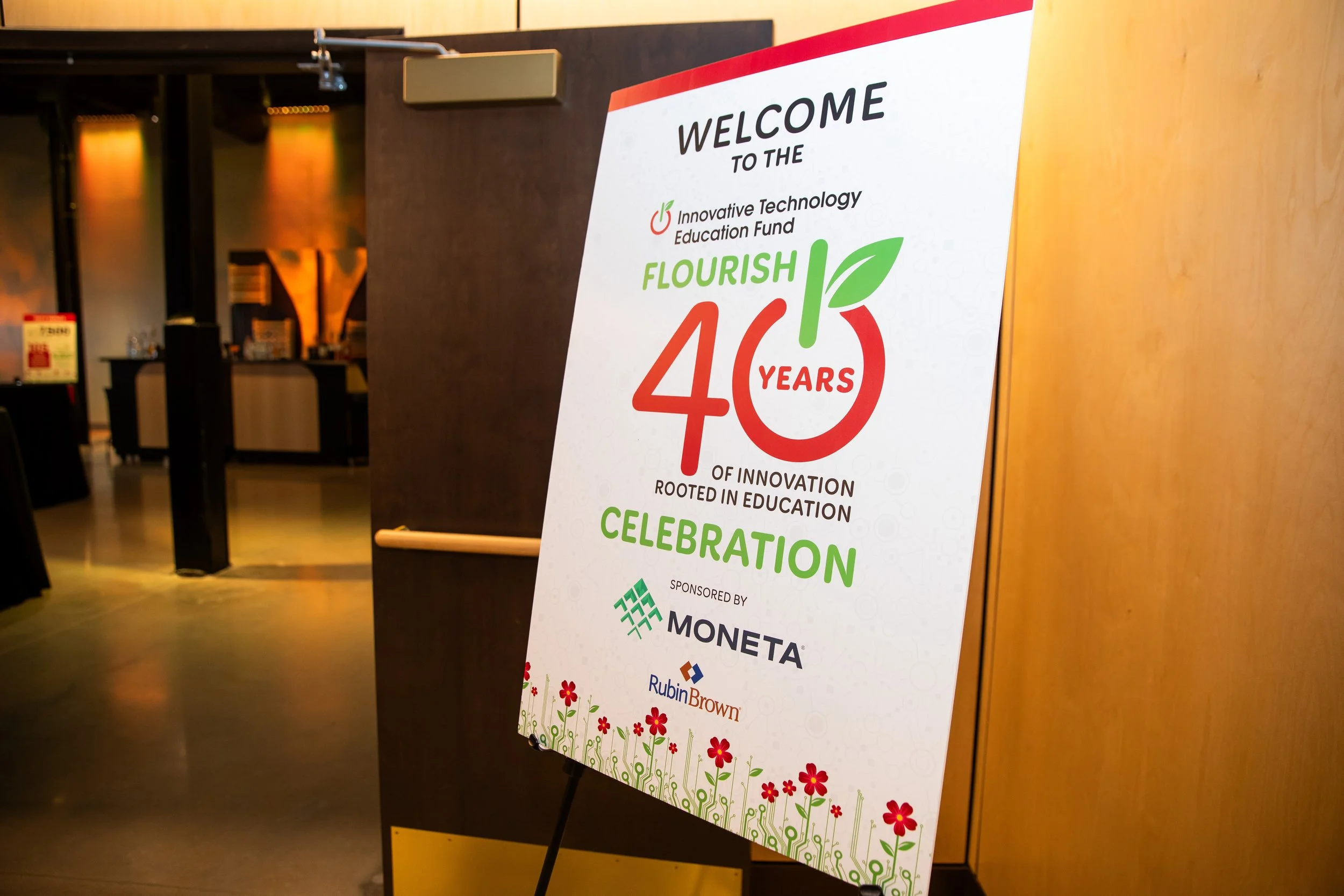A large white event sign on a black easel at a celebration event. The sign reads "Welcome to the Innovative Technology Education Fund Flourish 40 Years of Innovation Rooted in Education Celebration" with logos of sponsors at the bottom, including Mon