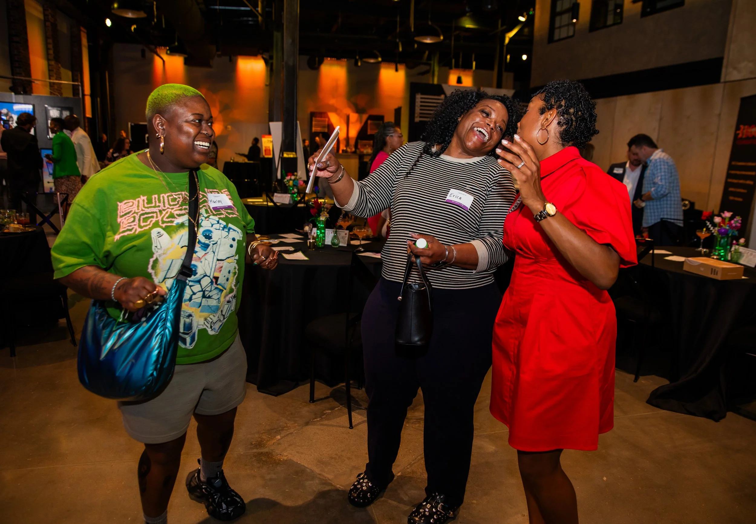 Three women socializing and laughing indoors at an event or gathering.
