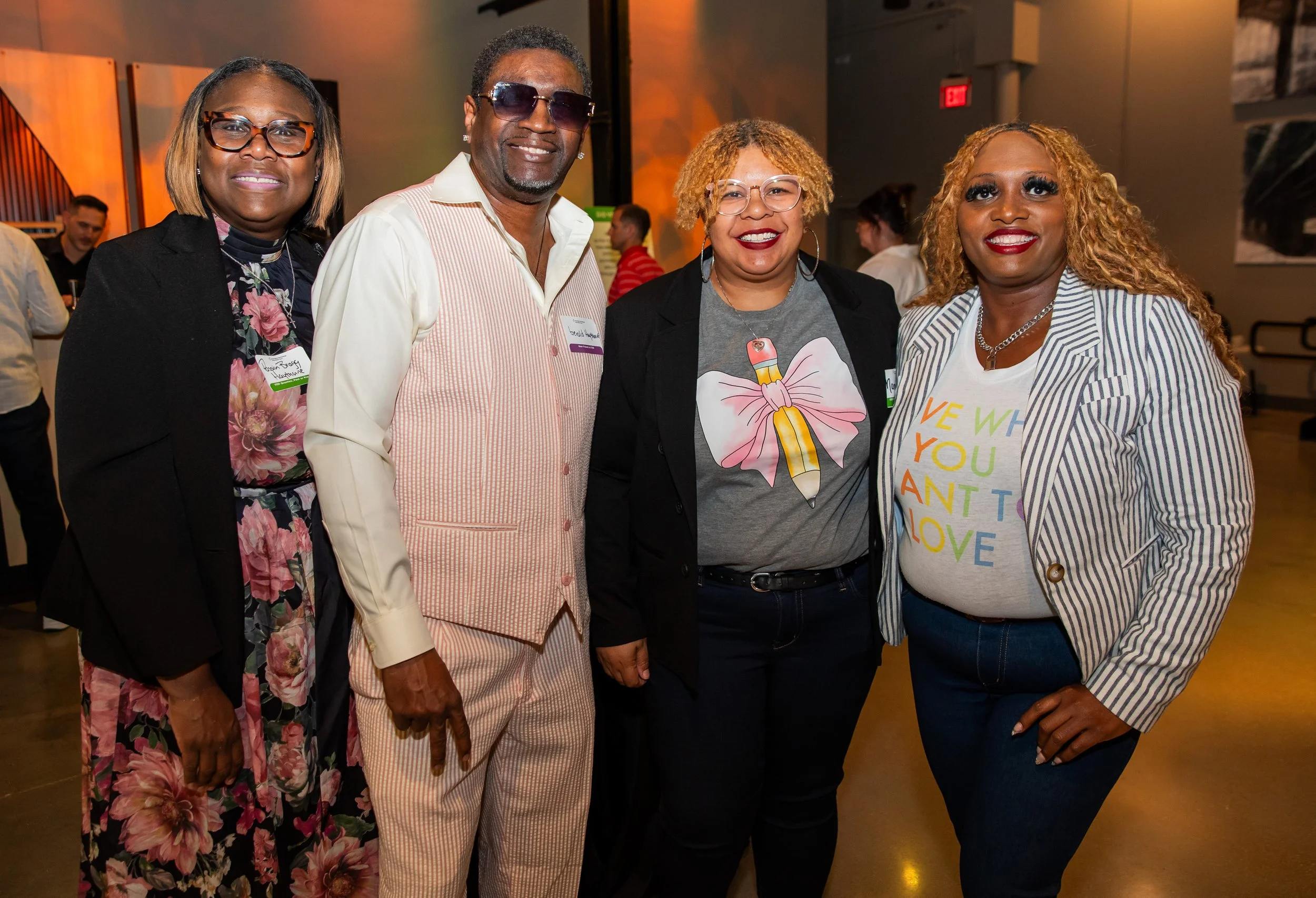 Four adults, three women and one man, standing together at an indoor event, smiling for the camera.