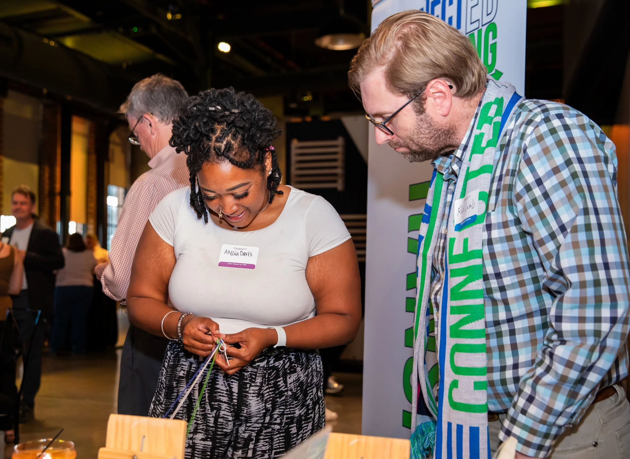 Women and man engaging in a conversation at a public event, with people in the background.
