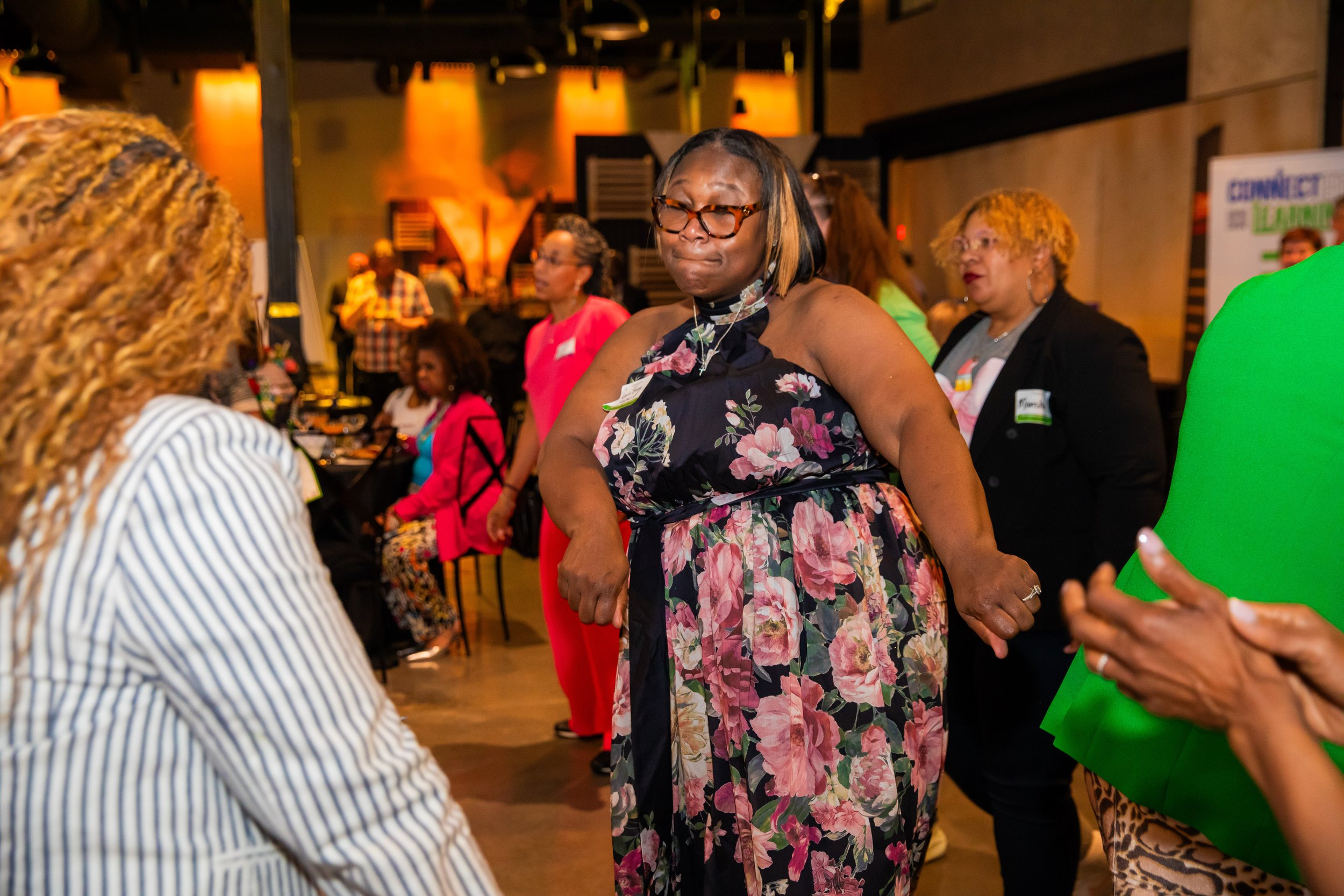 Women at a social gathering, dancing and interacting in a warmly lit indoor venue.
