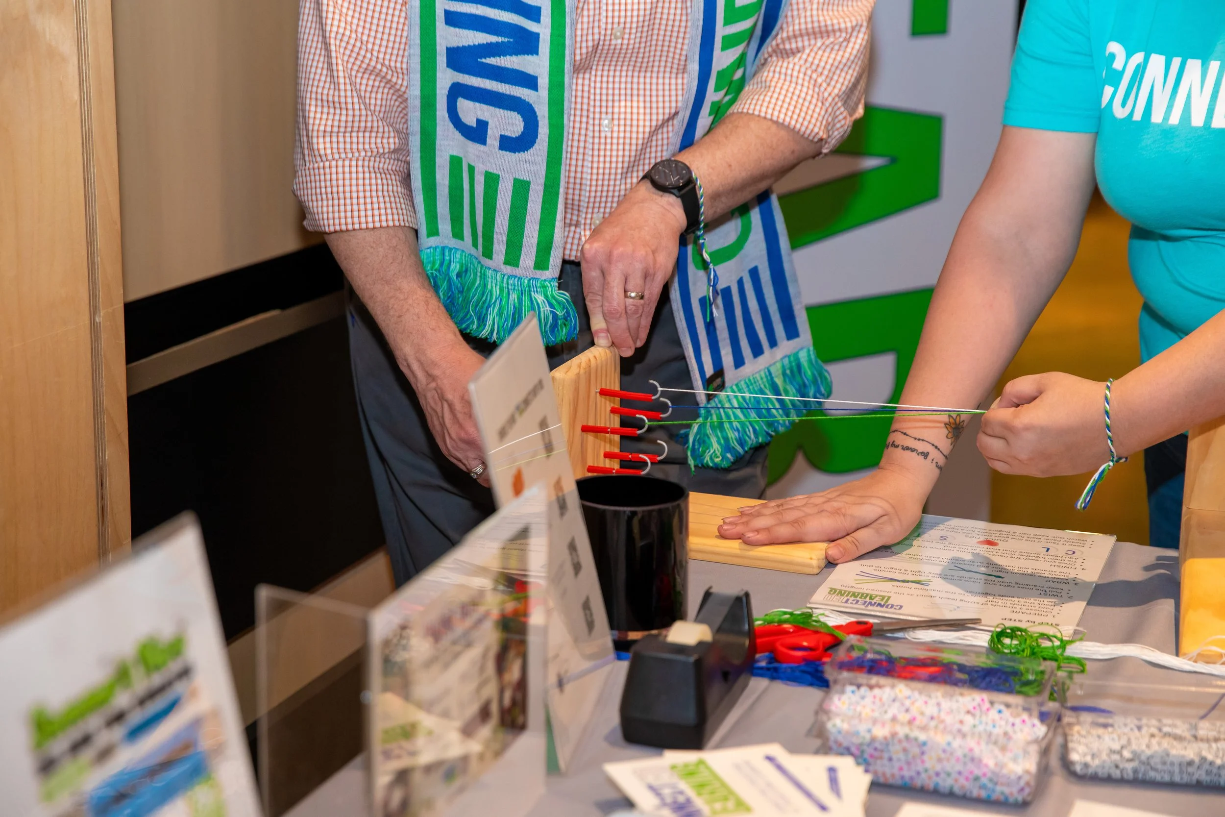 People at a table with colorful crafting supplies, including rubber bands, scissors, and informational pamphlets.