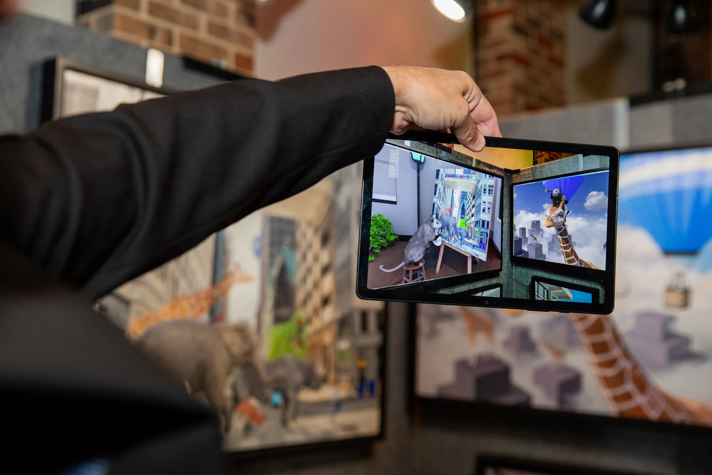 Person holding a tablet displaying an animated scene with animals including a giraffe and a mouse inside a building.