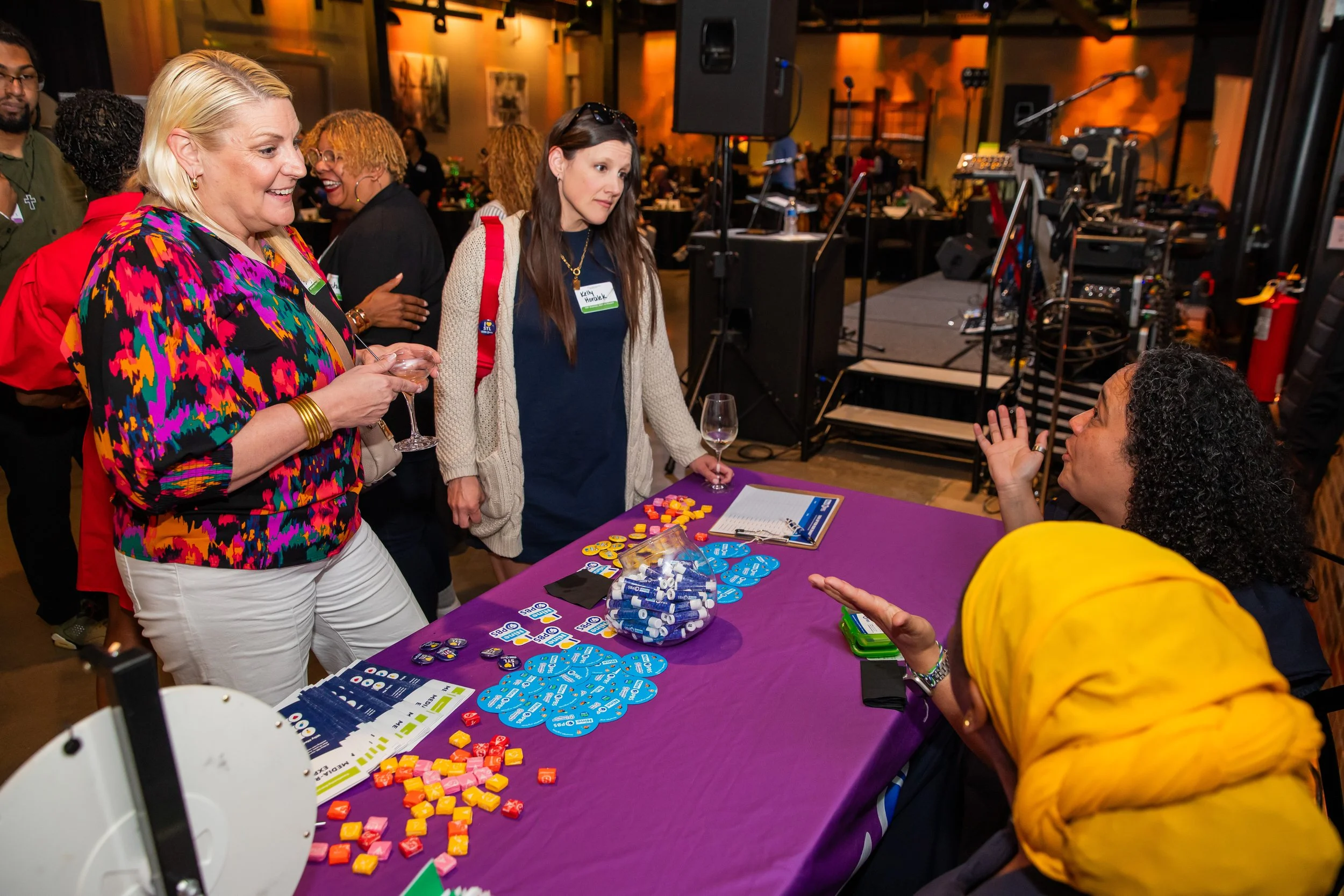 People gathered at a table with board game pieces, including chips, cards, and a score sheet, at an indoor event.