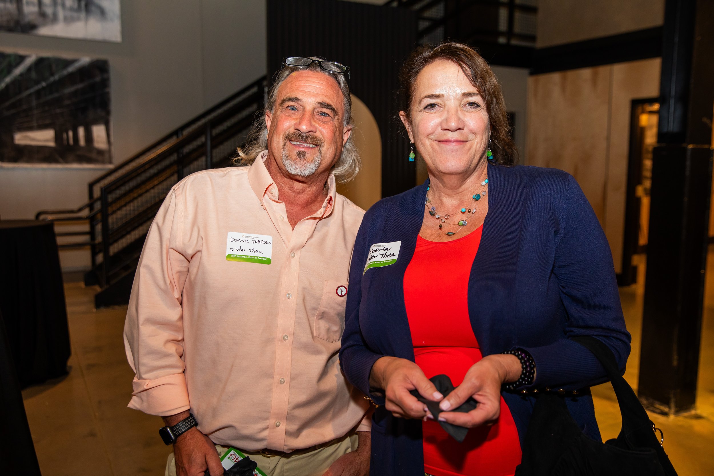 A man and a woman are standing together indoors and smiling at the camera.