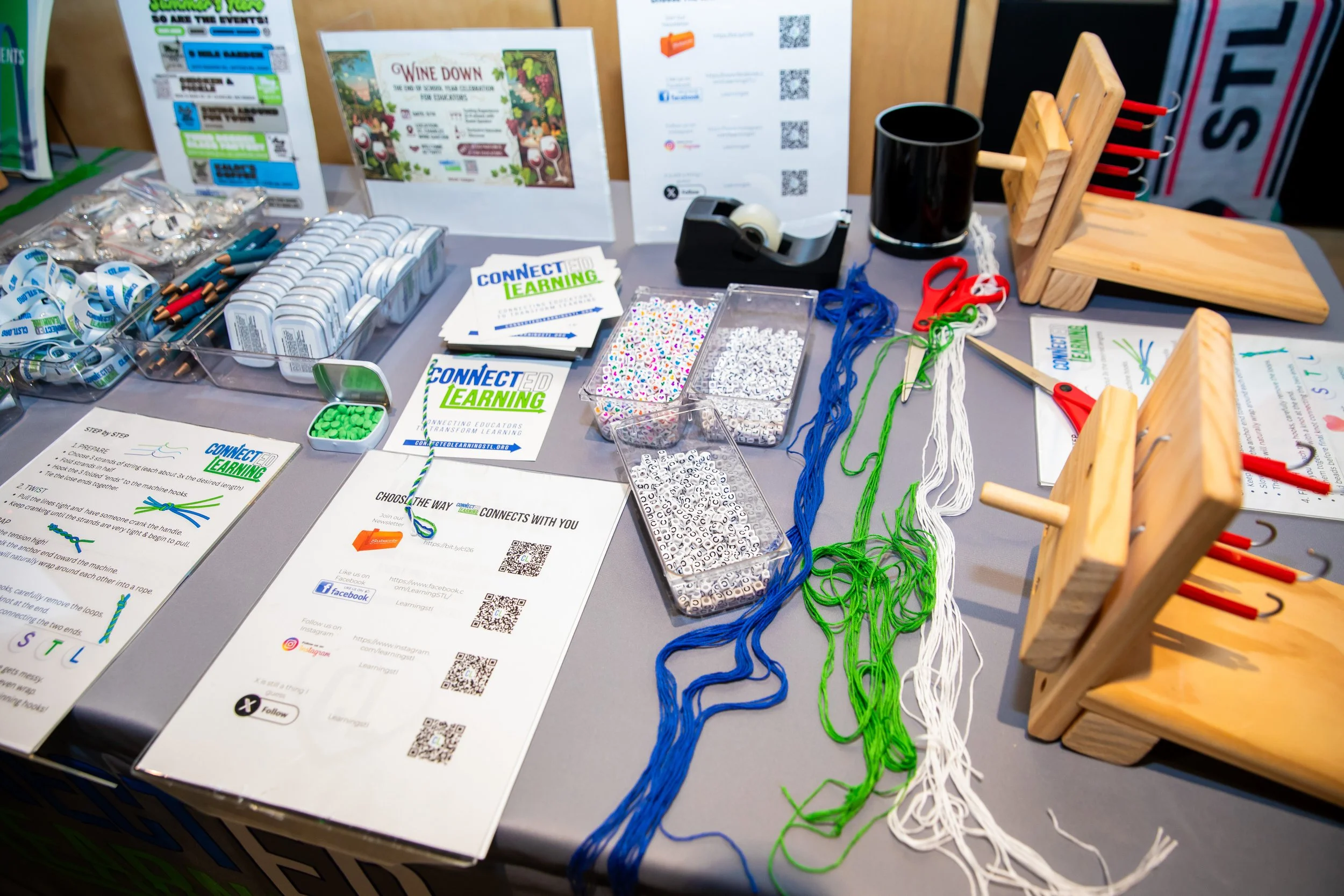 Table with educational materials, colorful strings, scissors, and promotional flyers for 'Connect Ed Learning' at an event.