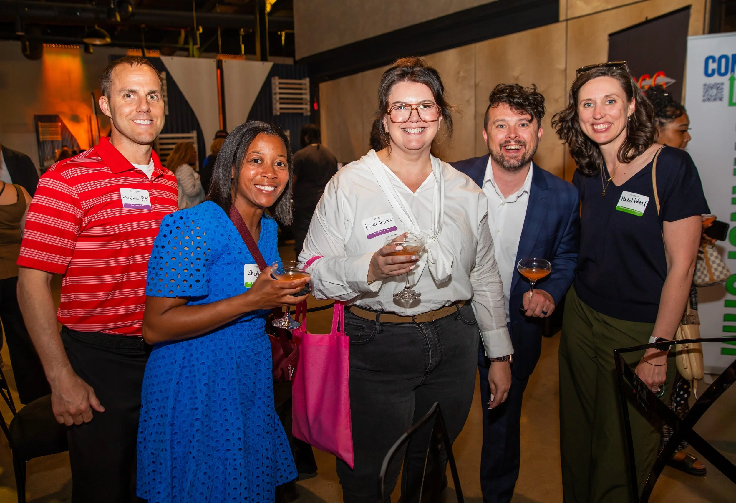 Group of five people smiling and holding drinks at an indoor social event.