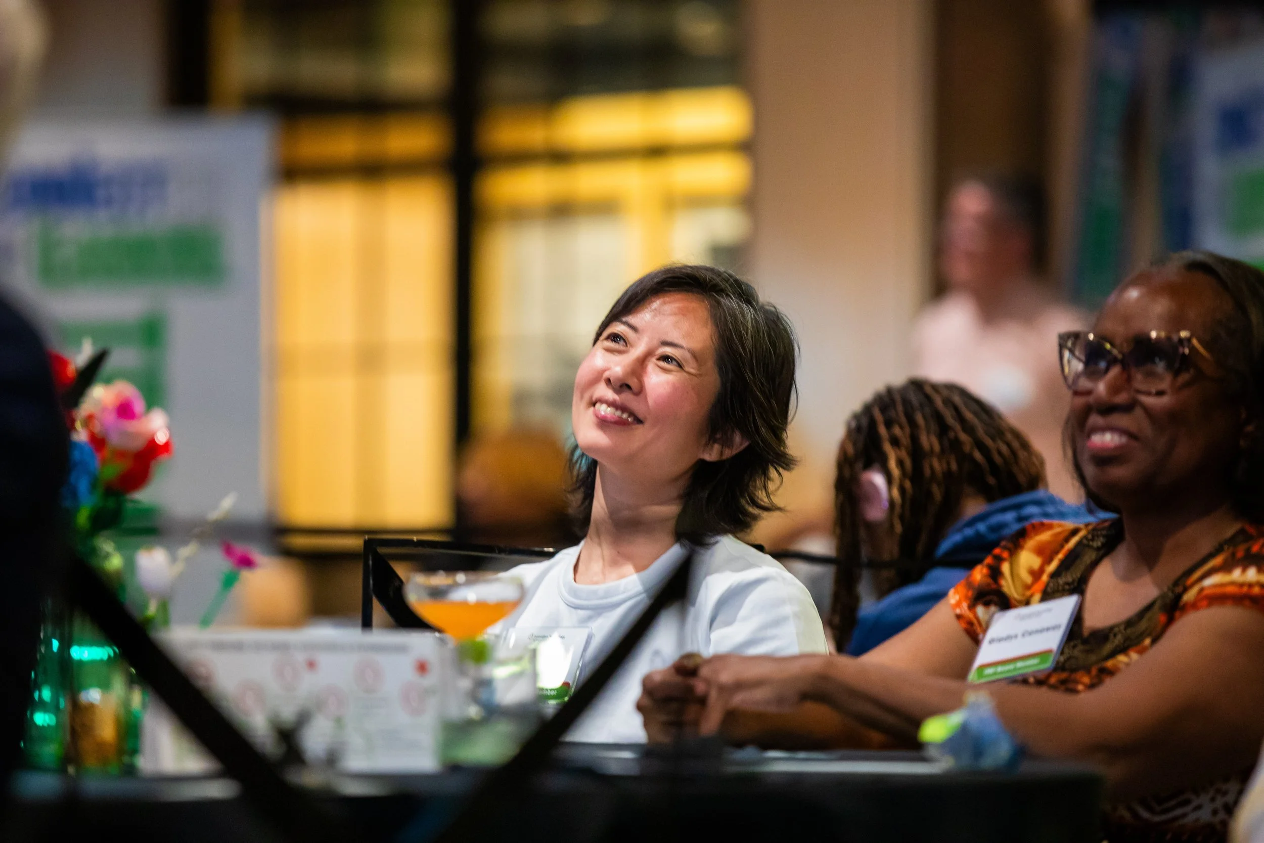 A group of women smiling and enjoying a social event or celebration, sitting at a table with drinks and decorations.
