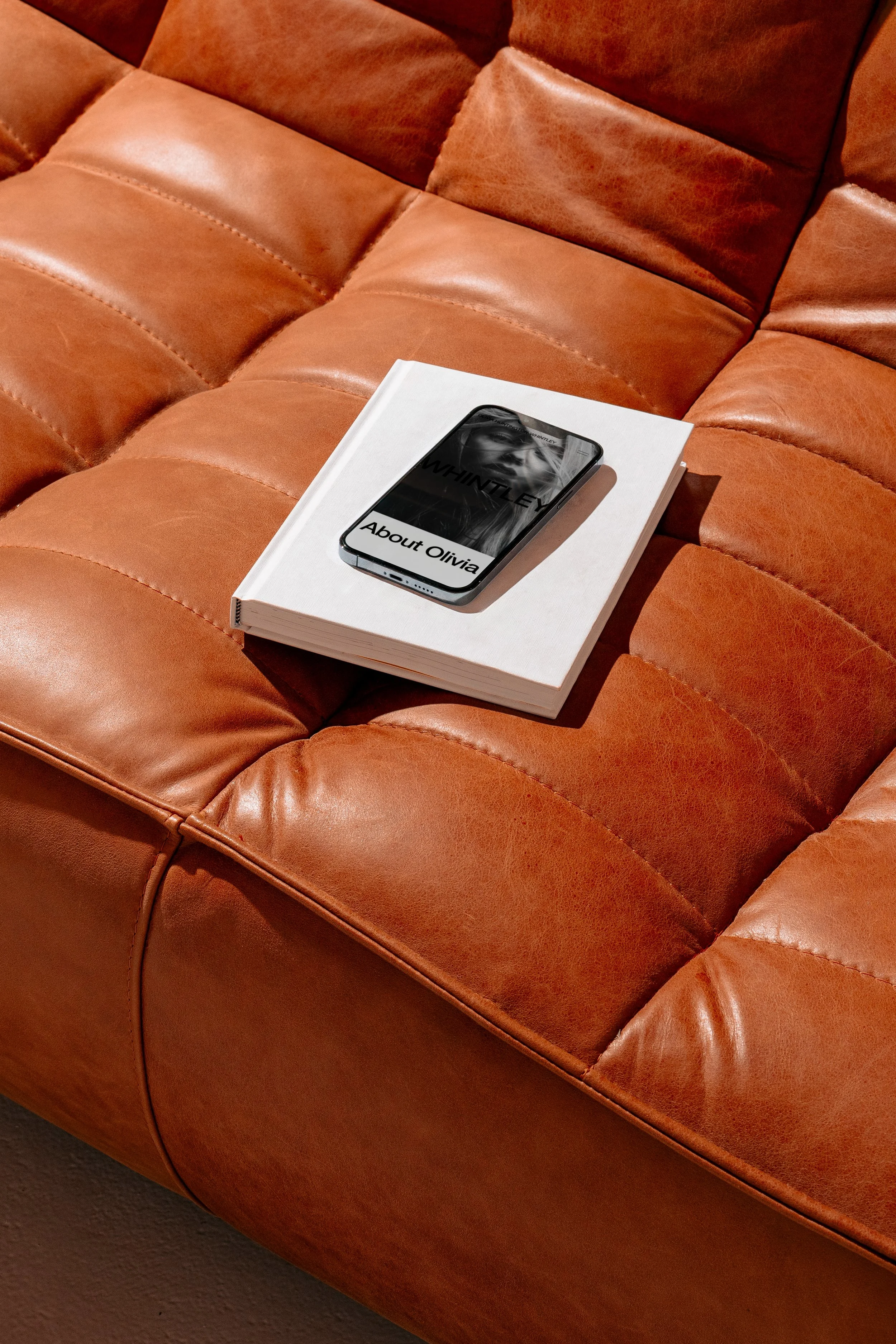 A brown leather sofa with a white book and a smartphone placed on top of it.