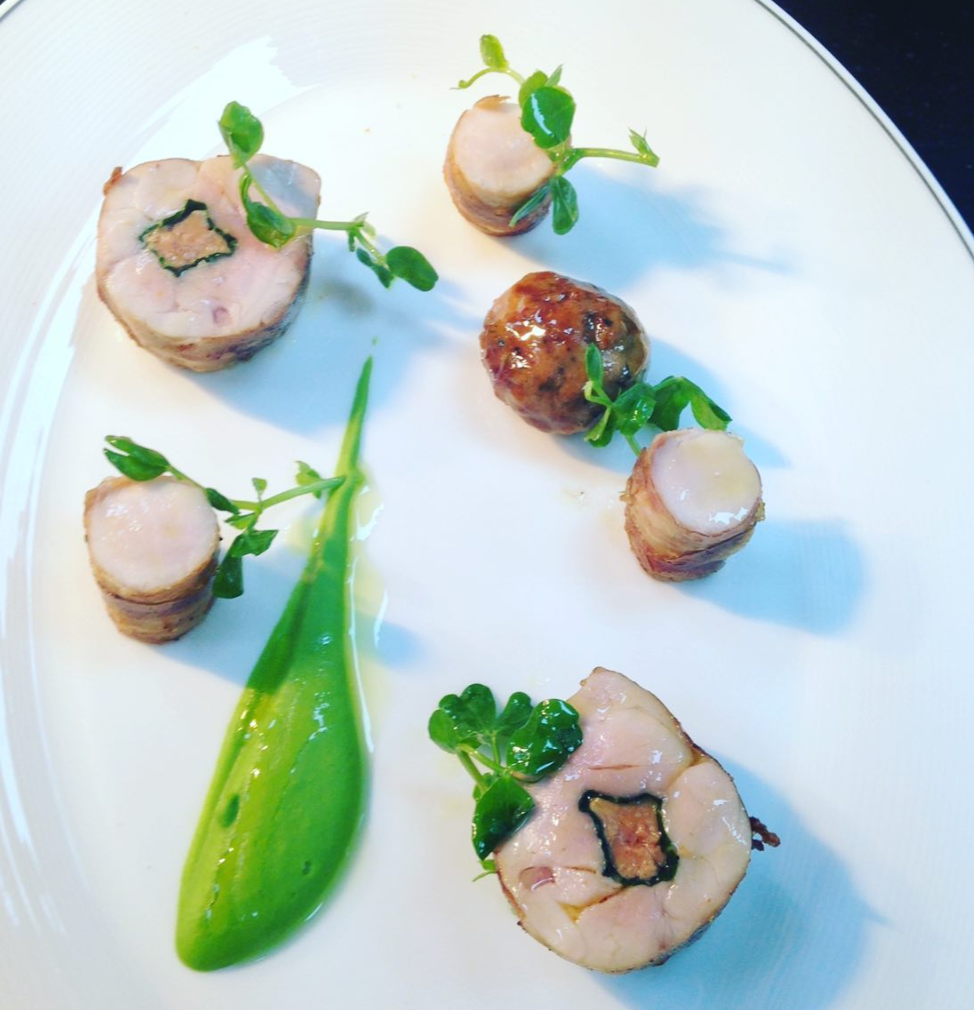 Plated gourmet dish with rolled meat slices garnished with microgreens, a meatball, and a green sauce on a white plate.