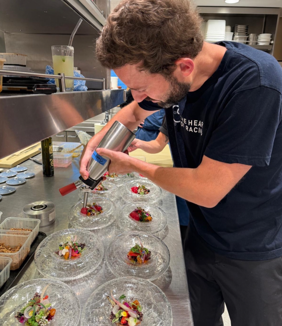 Chef garnishing plated dishes with spray can in a professional kitchen.